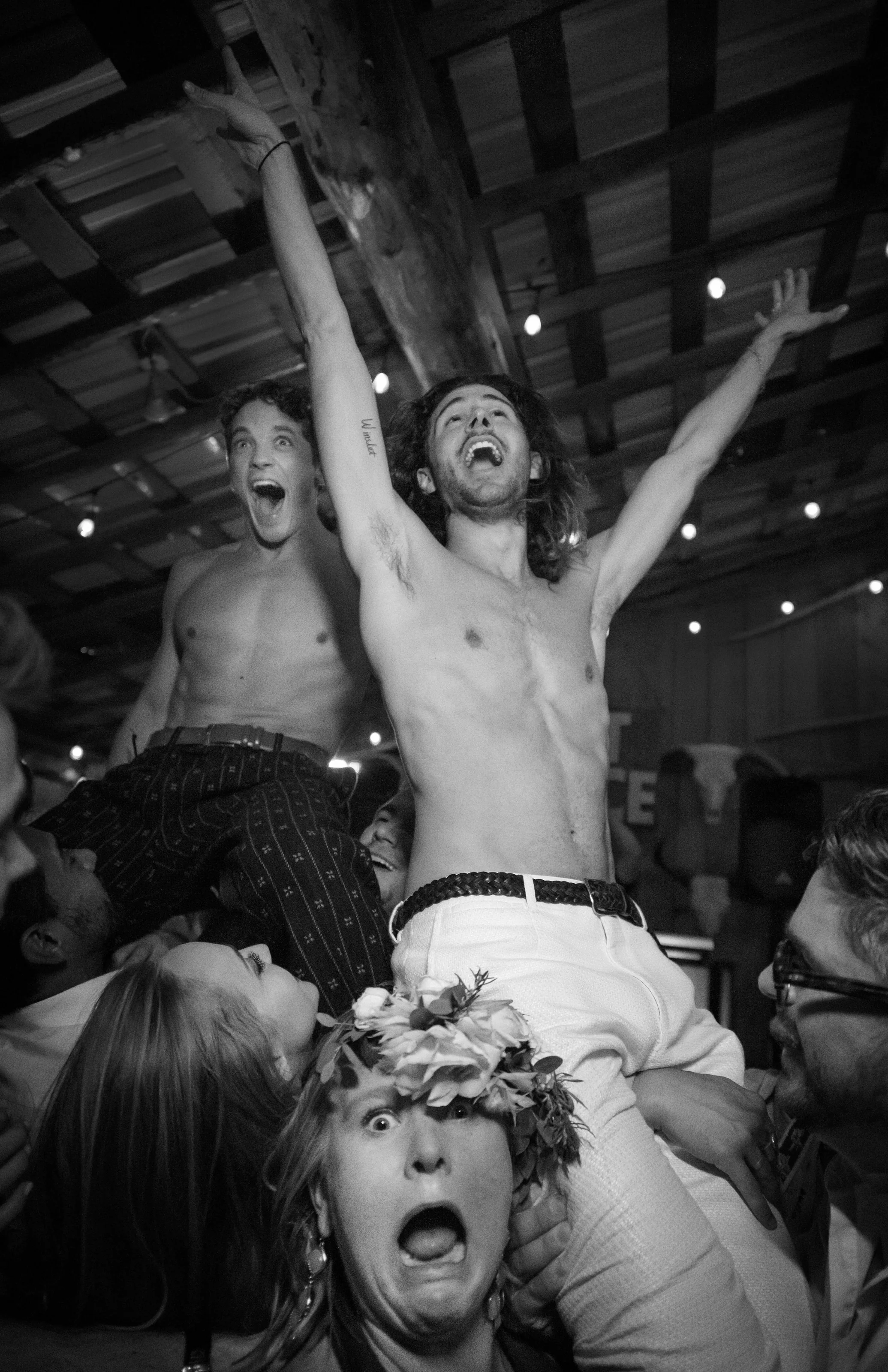 In black and white, two grooms are lifted onto their guests' shoulders, arms high, as the dance floor erupts in Montana.