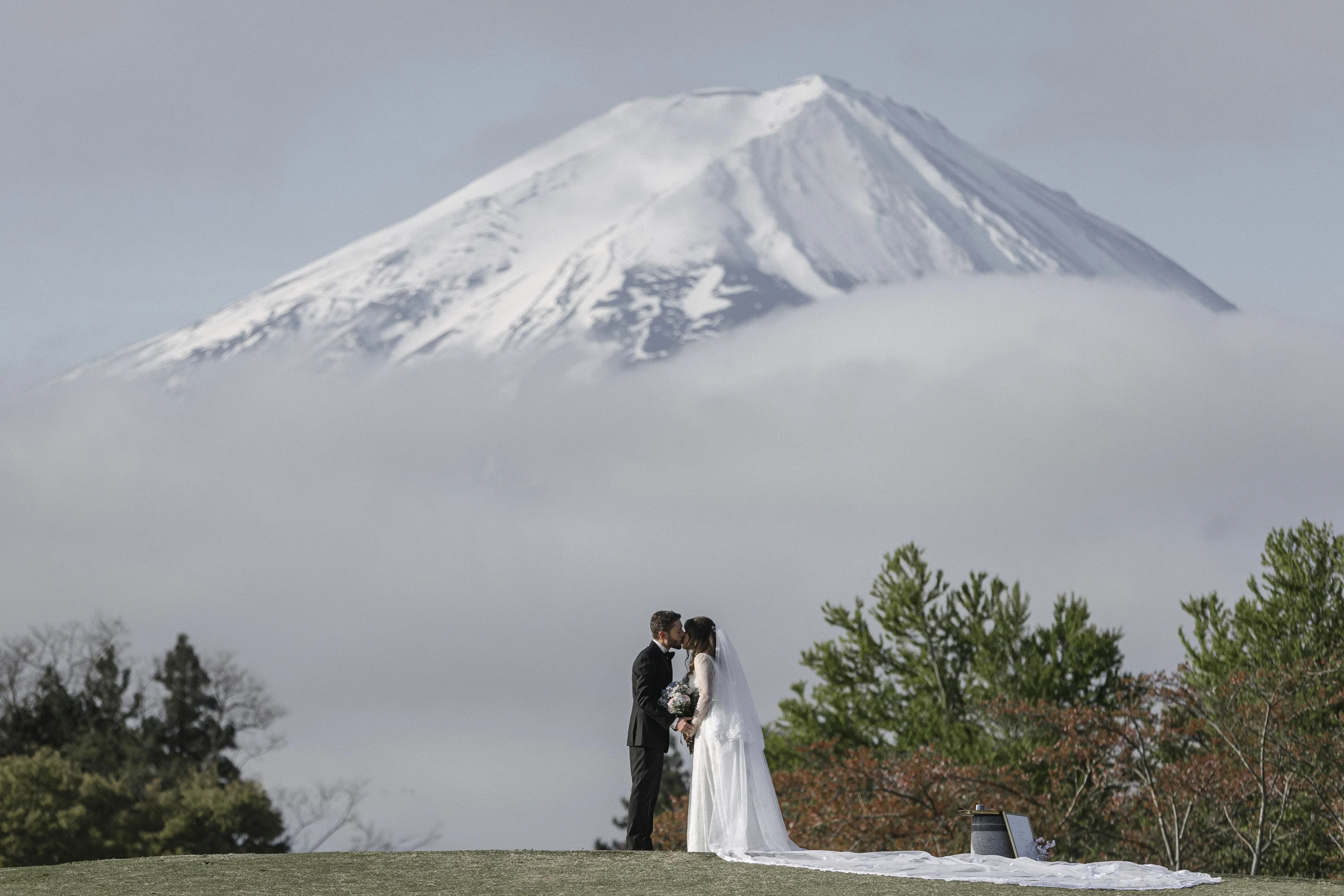 The couple kiss on a lawn by Lake Kawaguchi as Mt Fuji's summit rises out of a sea of cloud, at the end of their spring elopement vows.