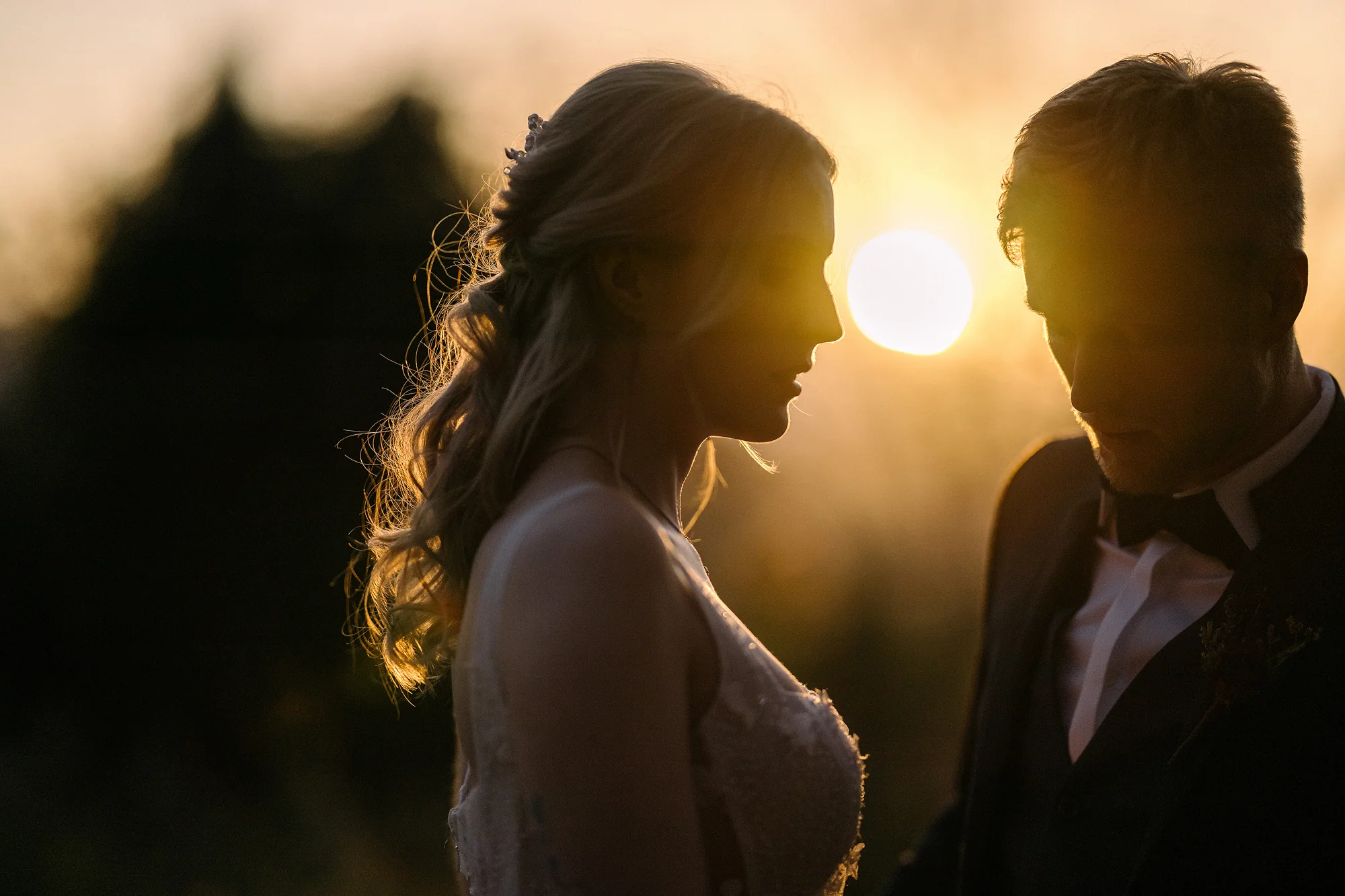 The couple face each other in silhouette as the sun sets between them.