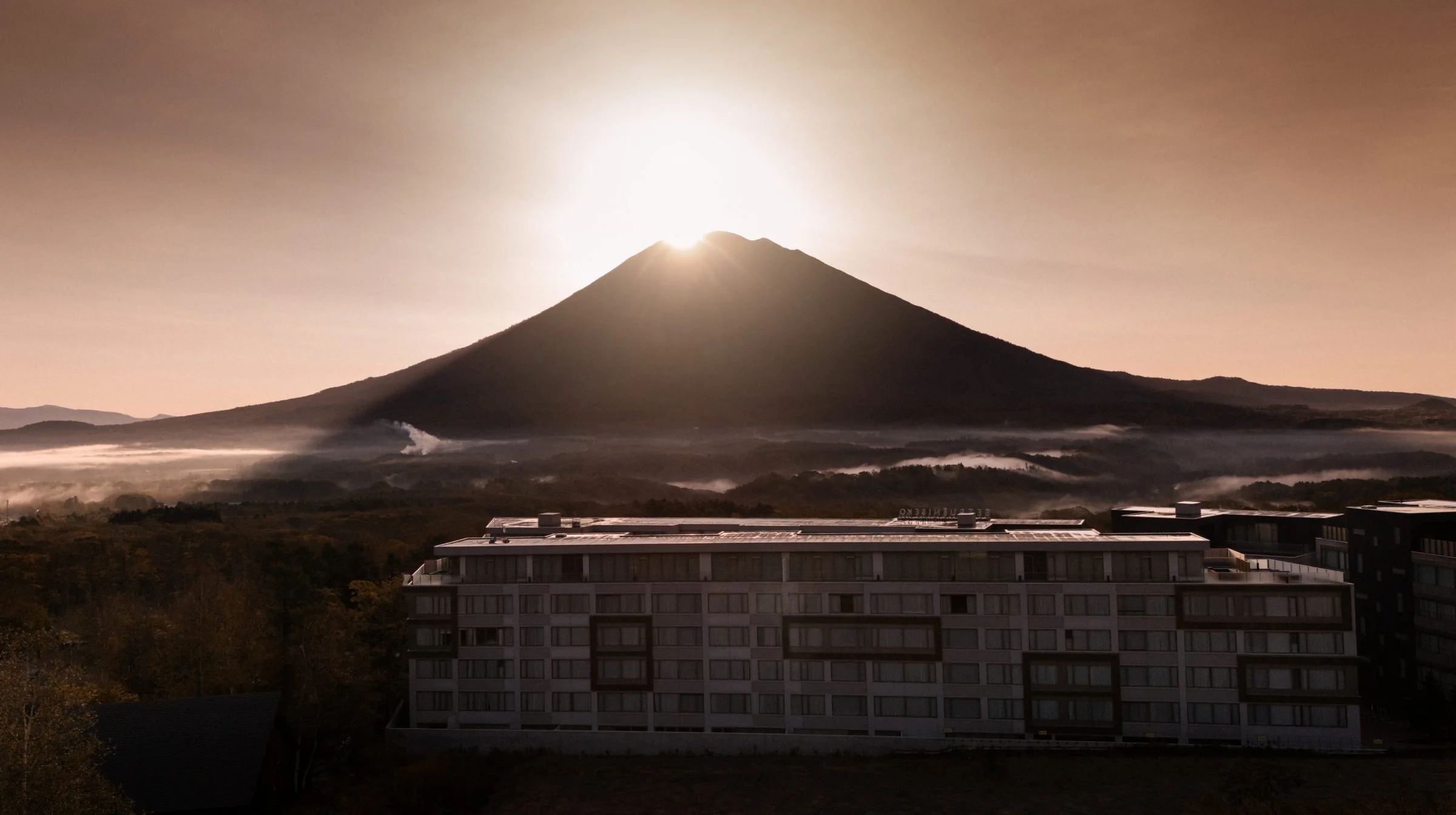 Morning sun breaking over the summit of Mount Yotei above Setsu Niseko and the autumn forest.