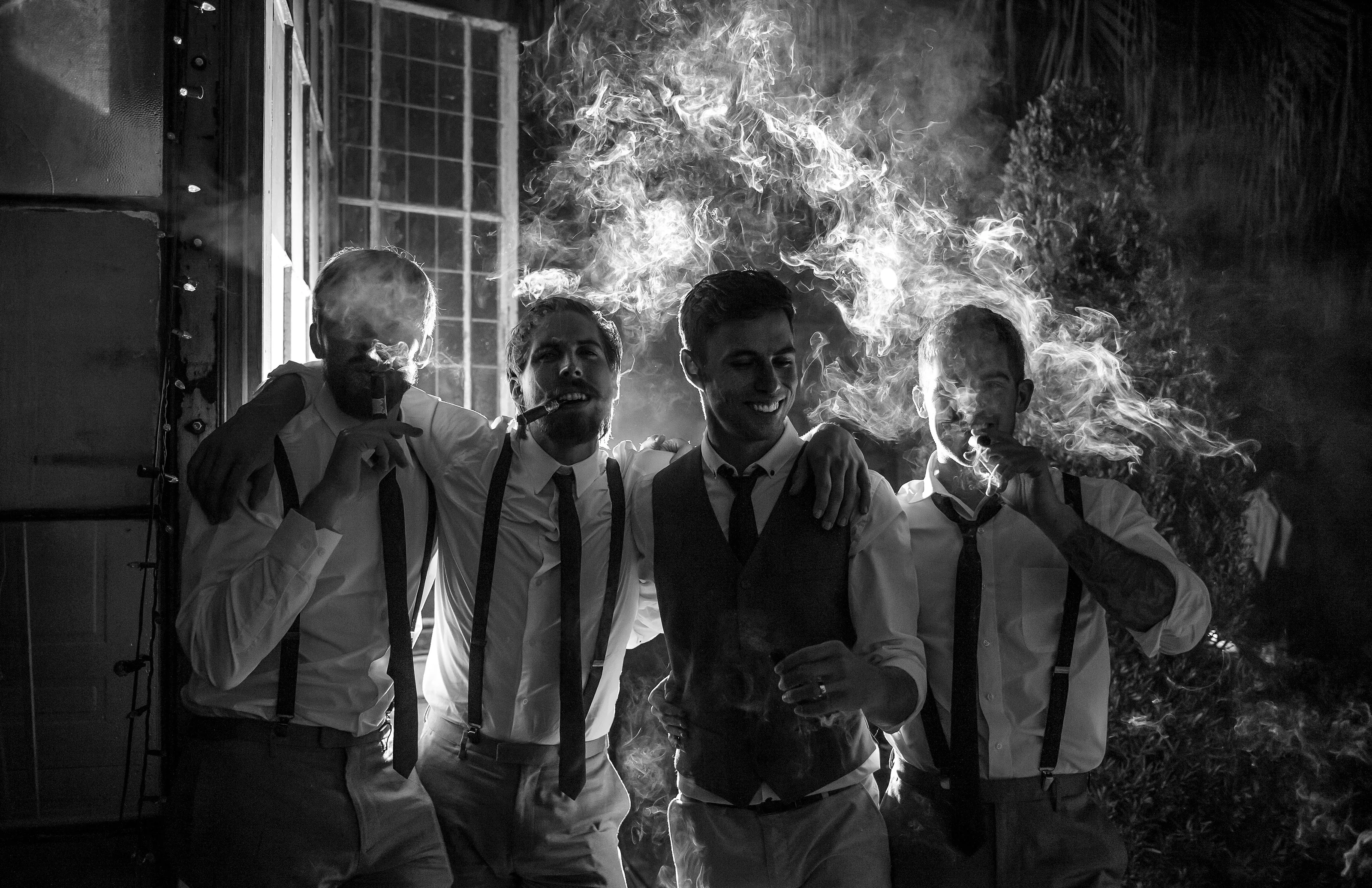 In black and white, the groom and his groomsmen laugh through clouds of cigar smoke in New Orleans.
