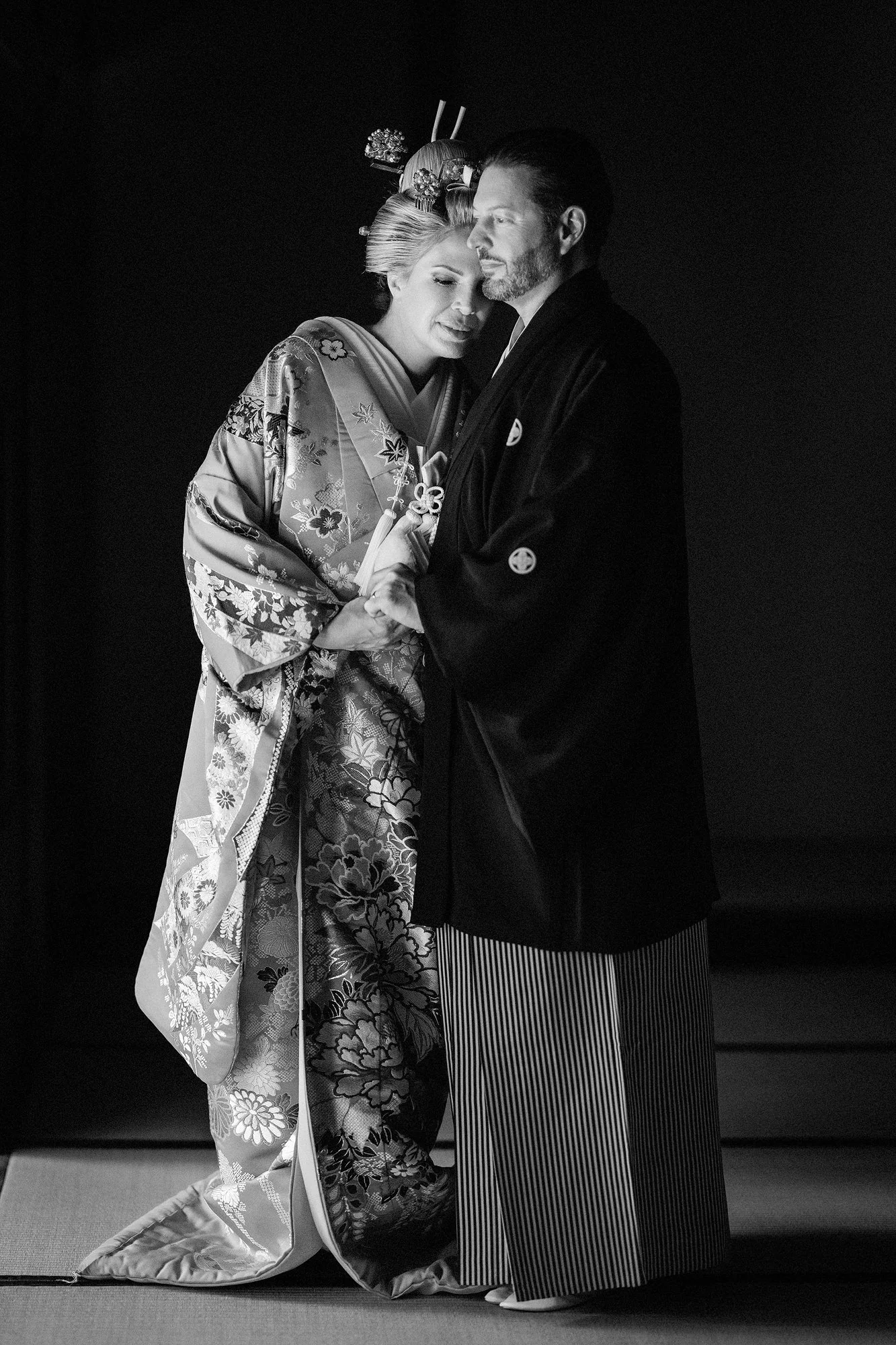 In black and white, a bride in nihongami and an embroidered uchikake stands with the groom.