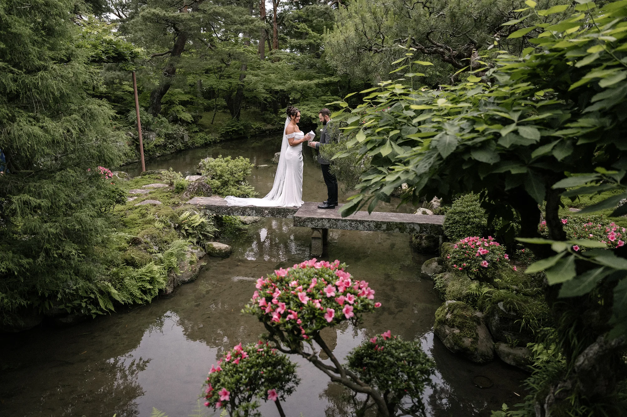 The couple stand on a stone bridge over a garden pond edged with azaleas in Niigata.