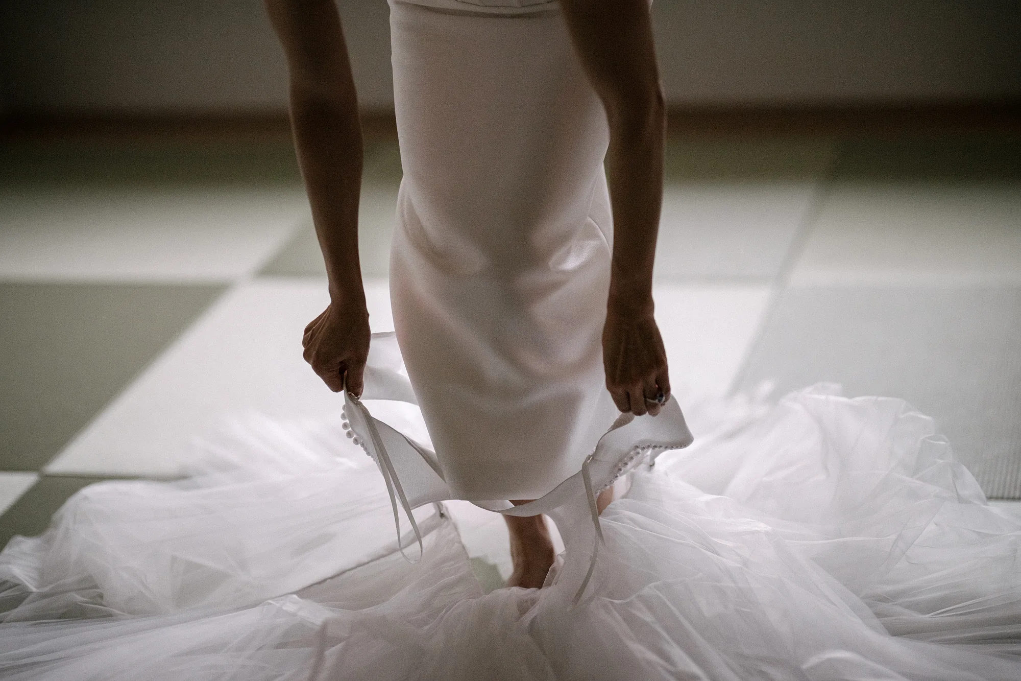 The bride lifts her gown as she crosses a tatami floor, the tulle spread around her feet, in Niseko.