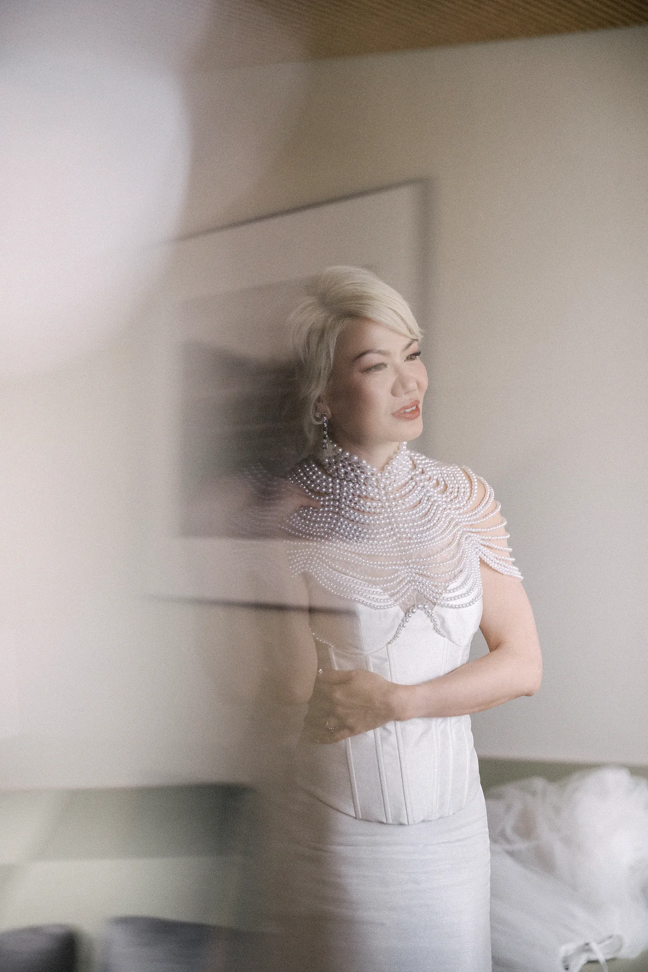 The bride in a pearl cape, seen softly in a mirror as she gets ready in Niseko.