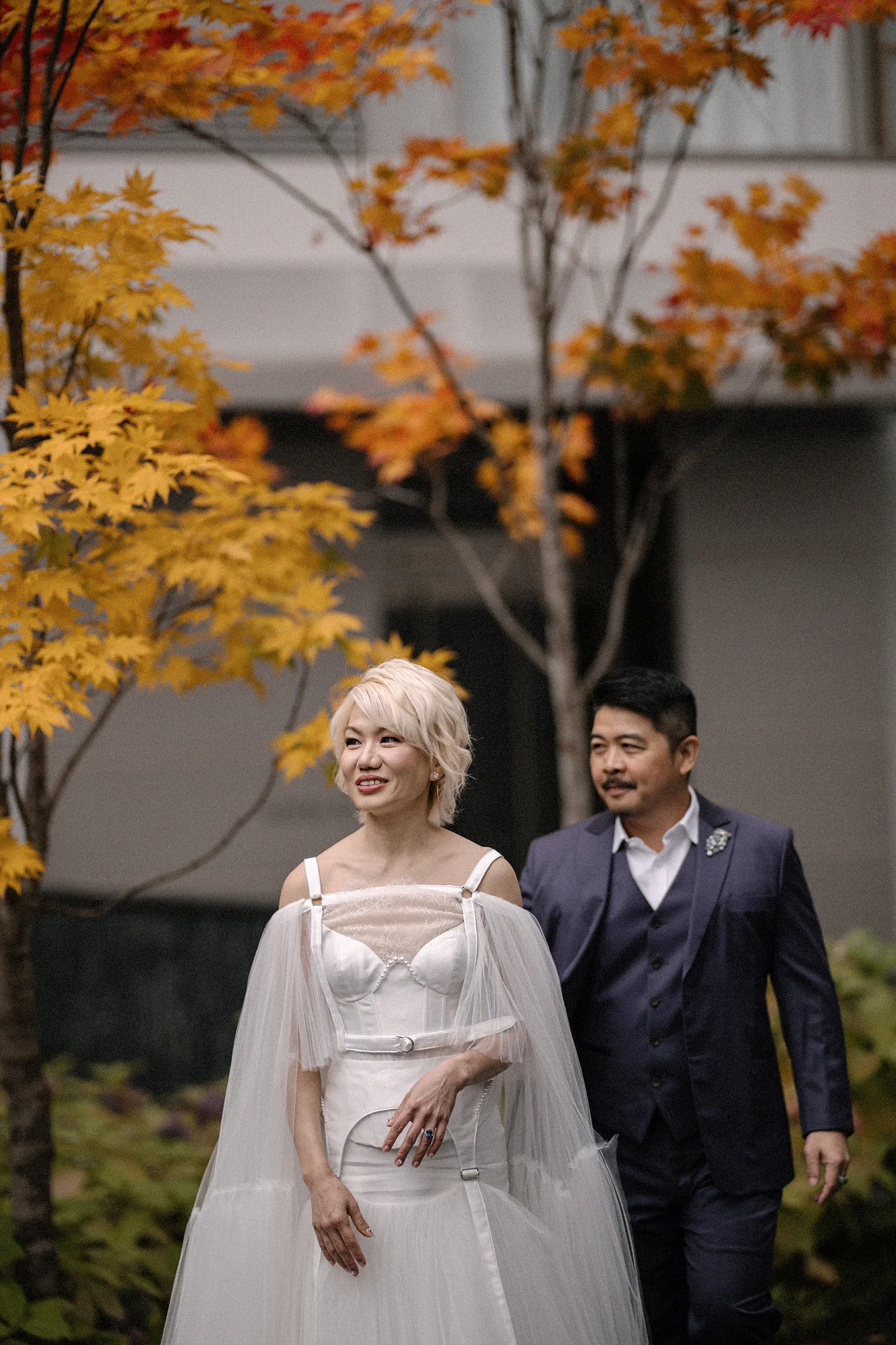 The couple walk beneath yellow and red maples in Niseko, the bride in a sheer cape.