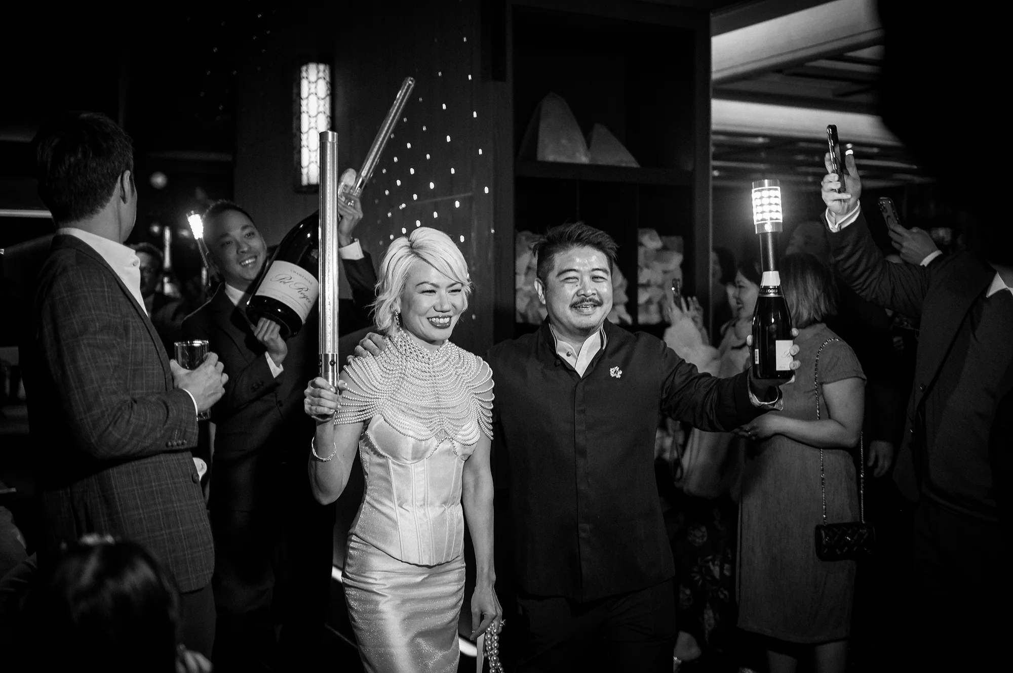 In black and white, the couple enter their reception as guests cheer and raise glowing bottles of champagne in Niseko.