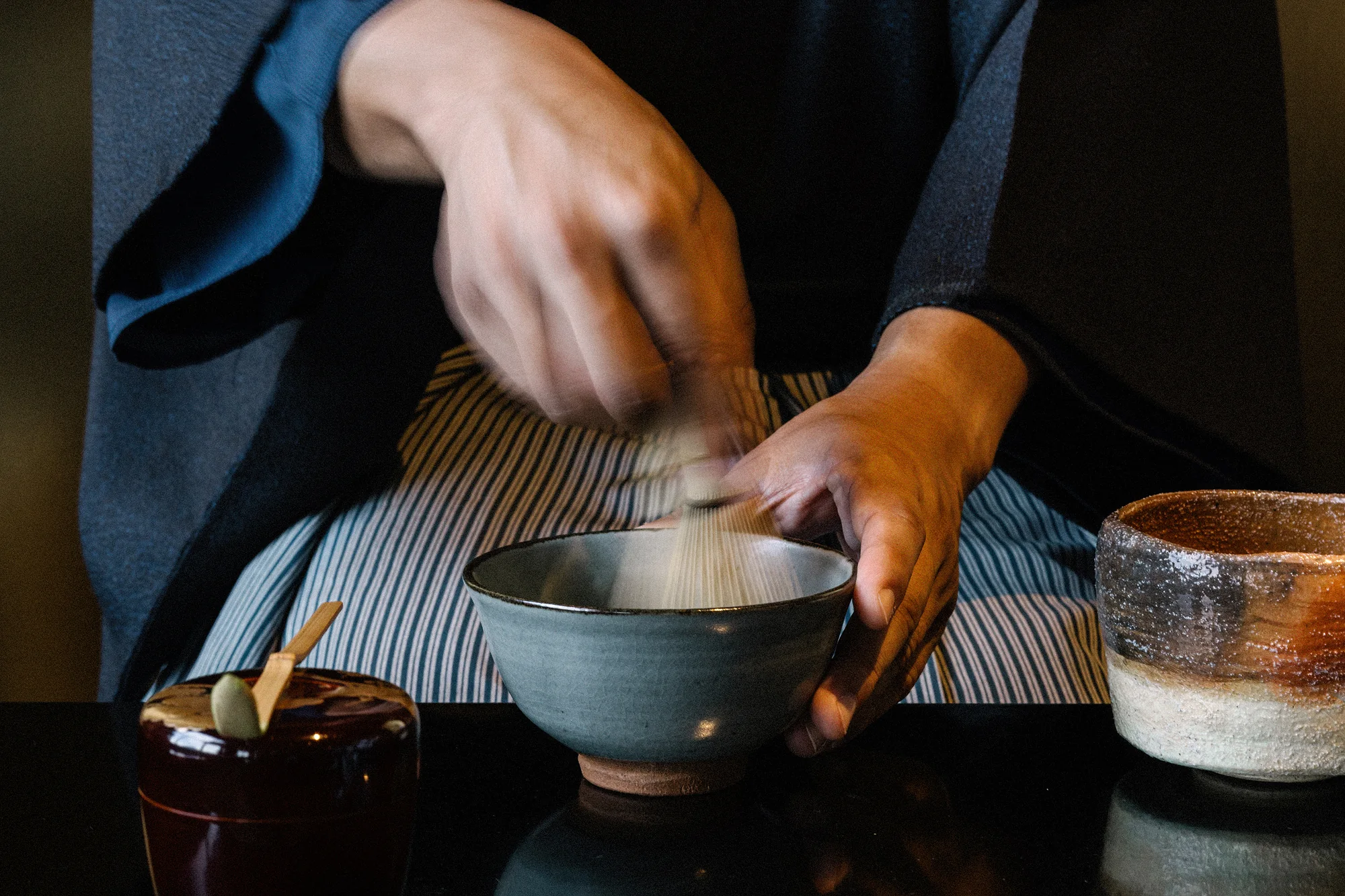 Hands whisk matcha in a pale blue bowl at a tea ceremony on the wedding weekend in Niseko.