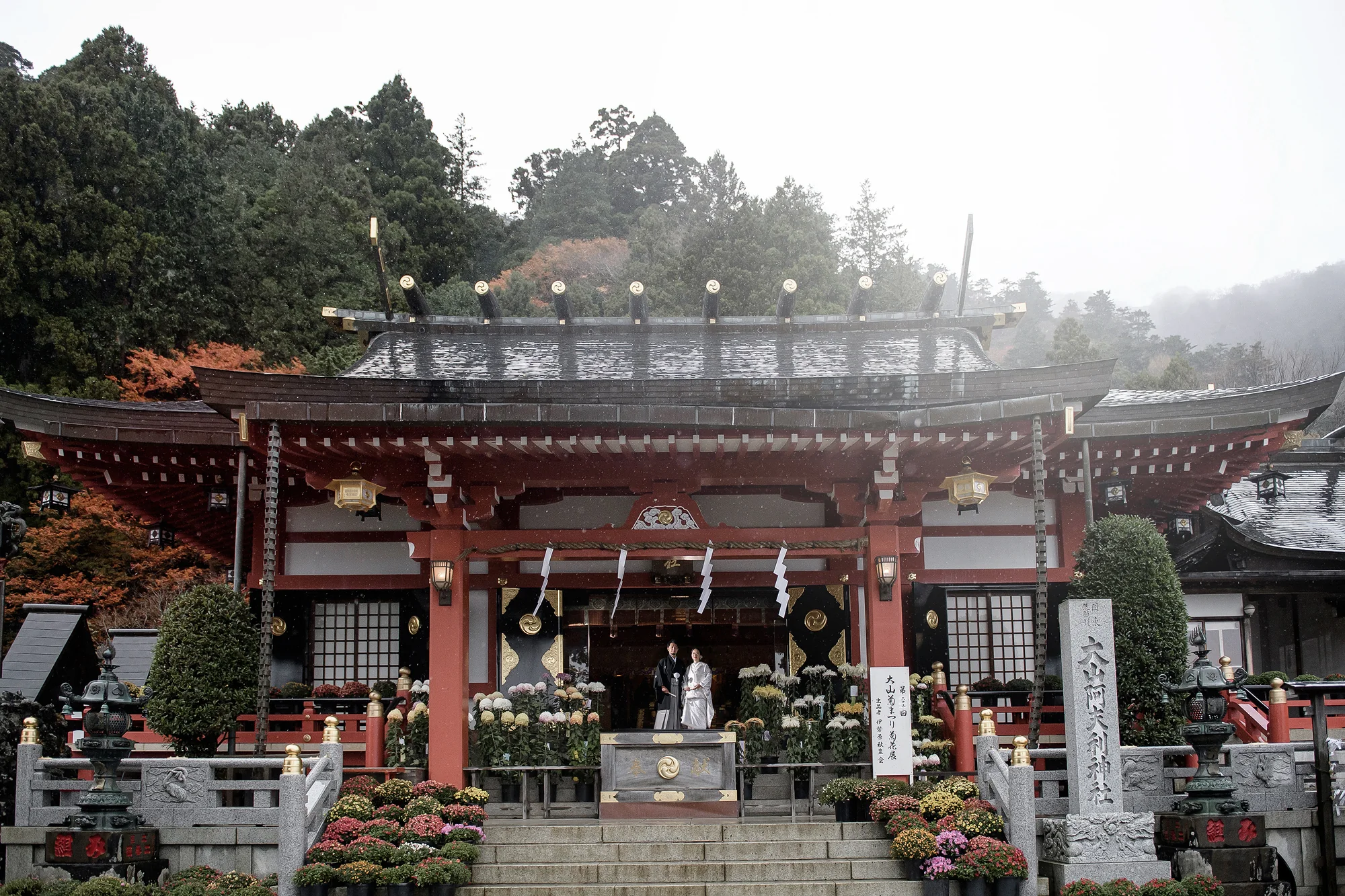 A couple before the red hall of Oyama Afuri Shrine in autumn.