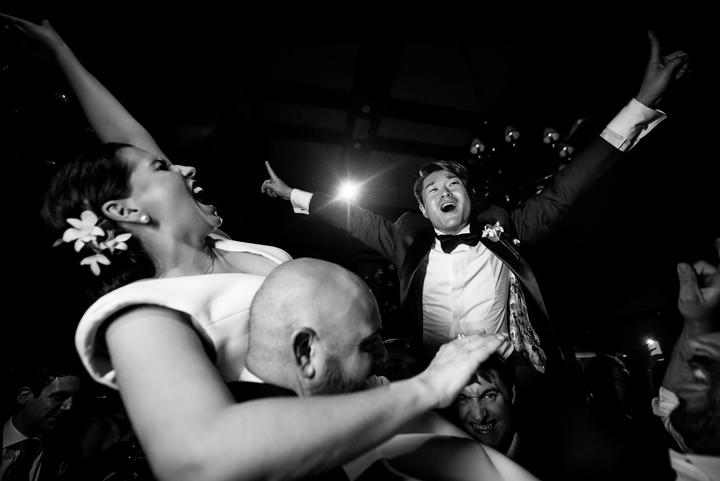 In black and white, the bride and groom are lifted onto their guests' shoulders, arms flung high, at their reception at the Park Hyatt Tokyo.