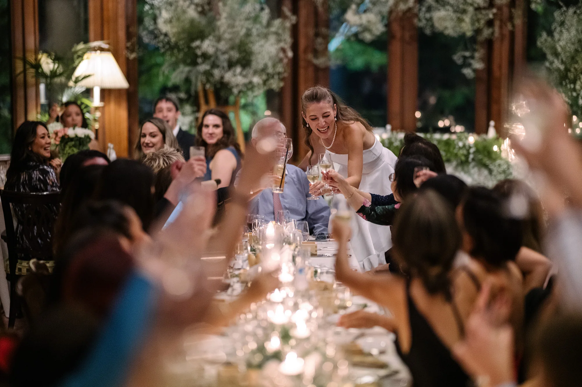 Guests raise their glasses along a candlelit reception table.