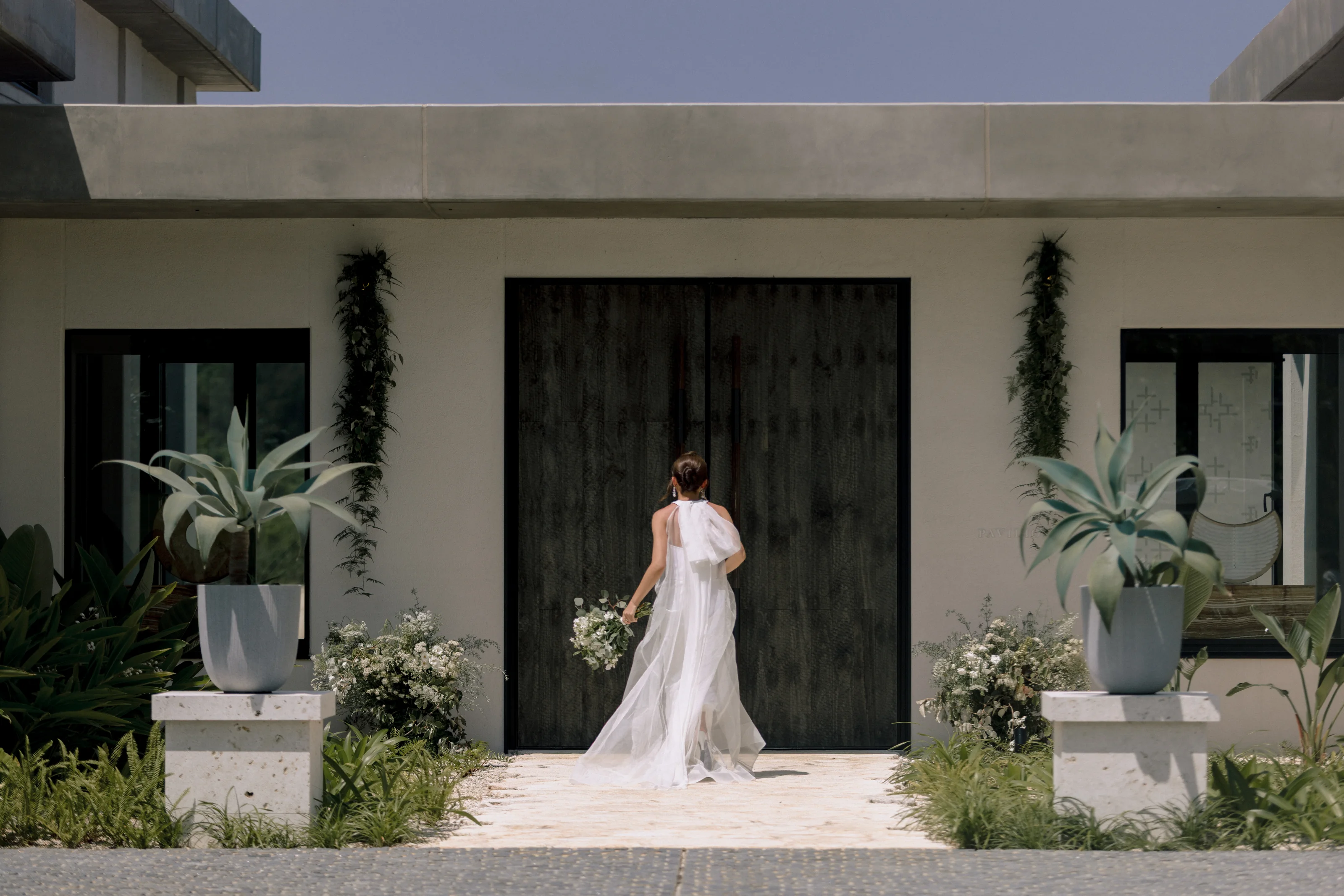 The bride walks up to the tall dark doors of a villa at Rosewood Miyakojima.