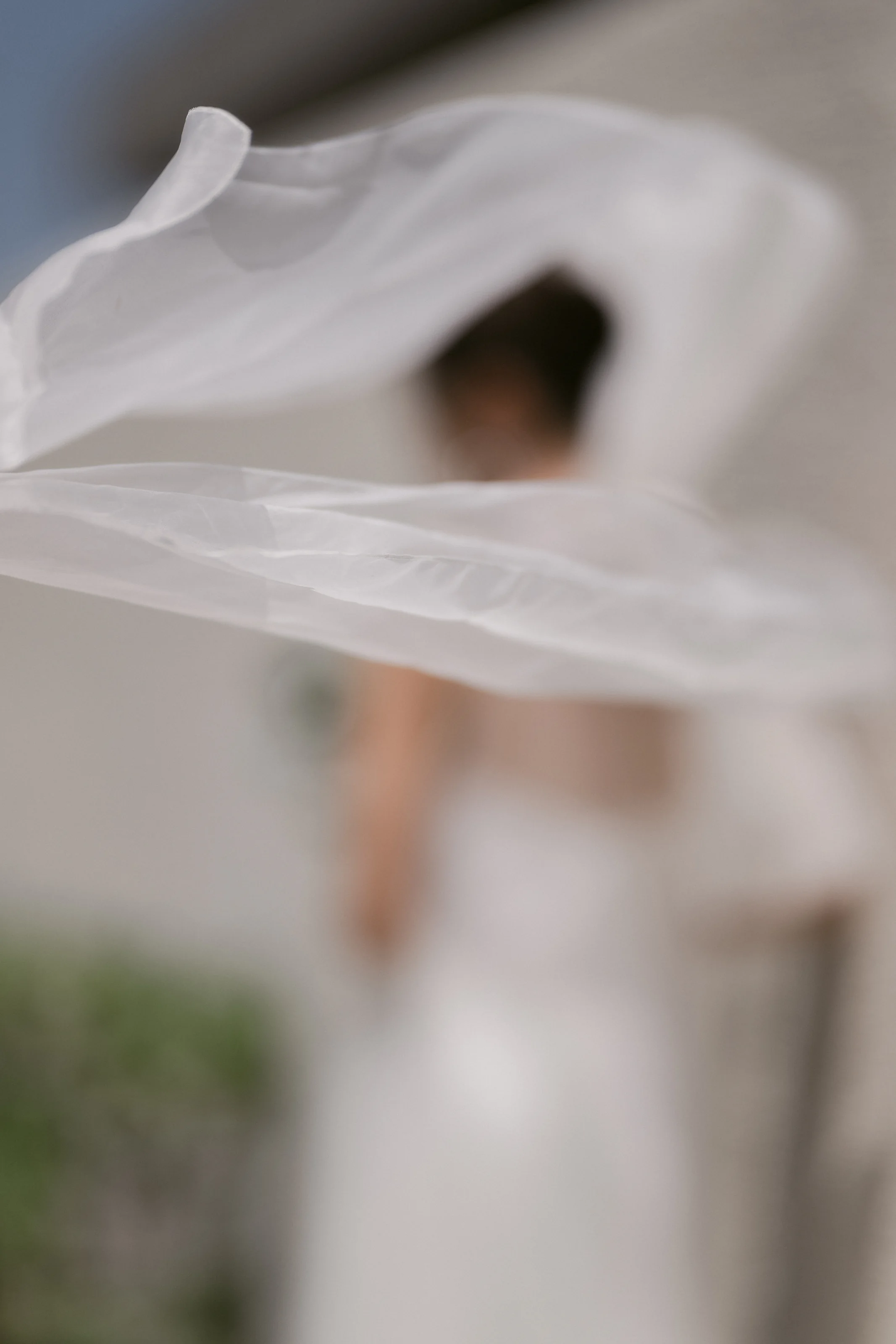 The bride's veil lifts in the wind in front of her, her figure soft behind it, at Rosewood Miyakojima.