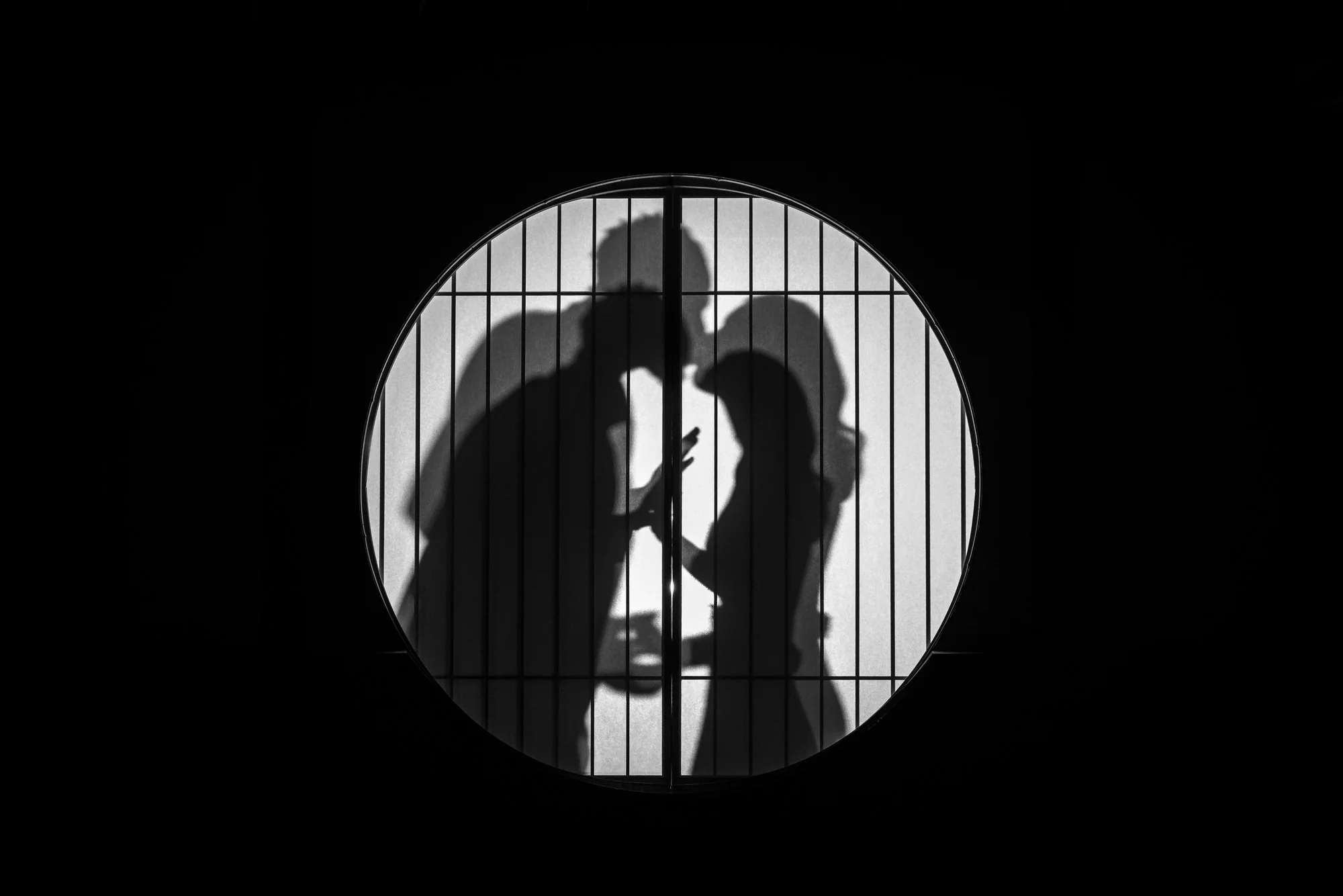 A couple in silhouette behind a round shoji window.