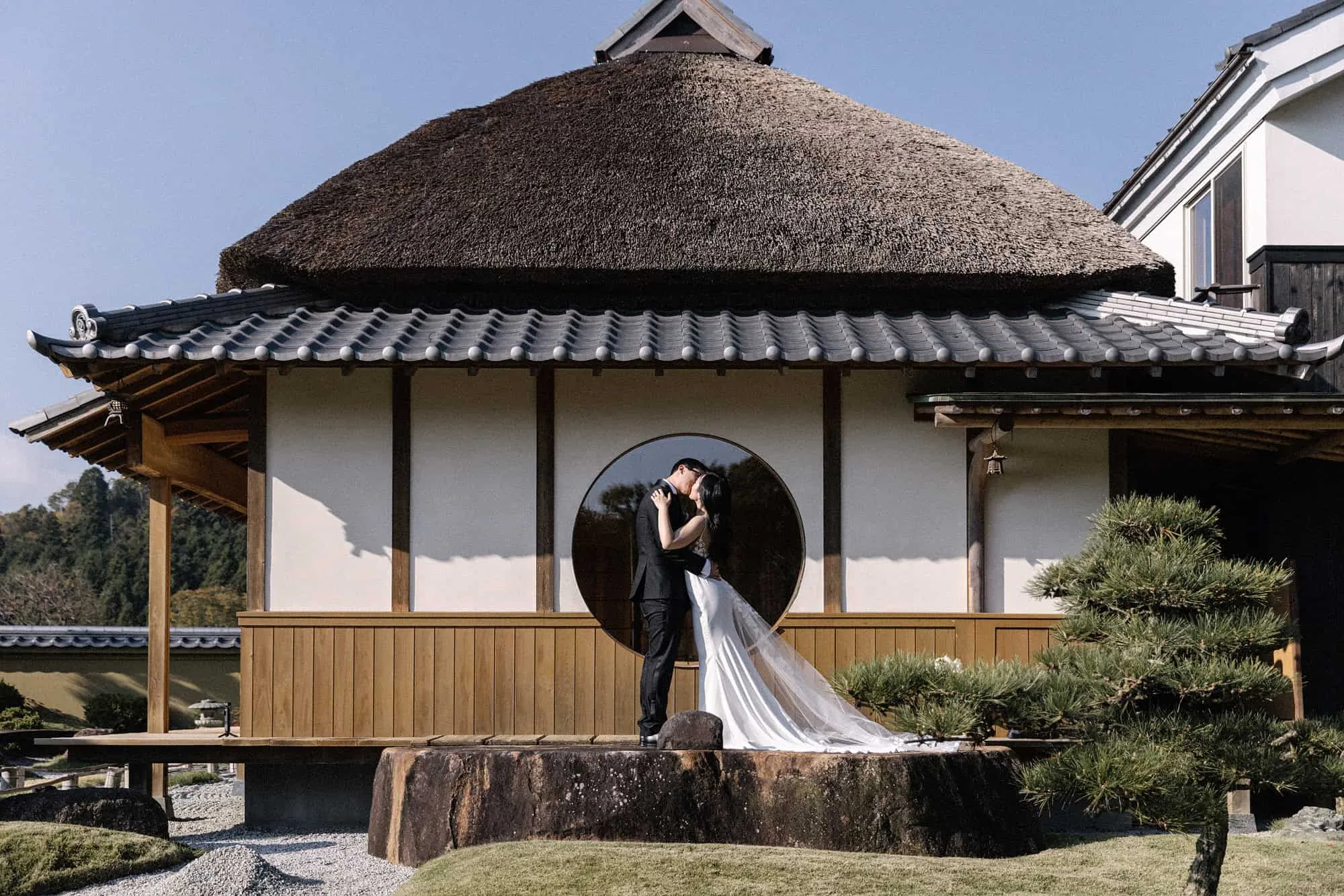 The couple kiss inside the round window of the thatched teahouse at Sasayuri Ann, her train falling over the stone step below.