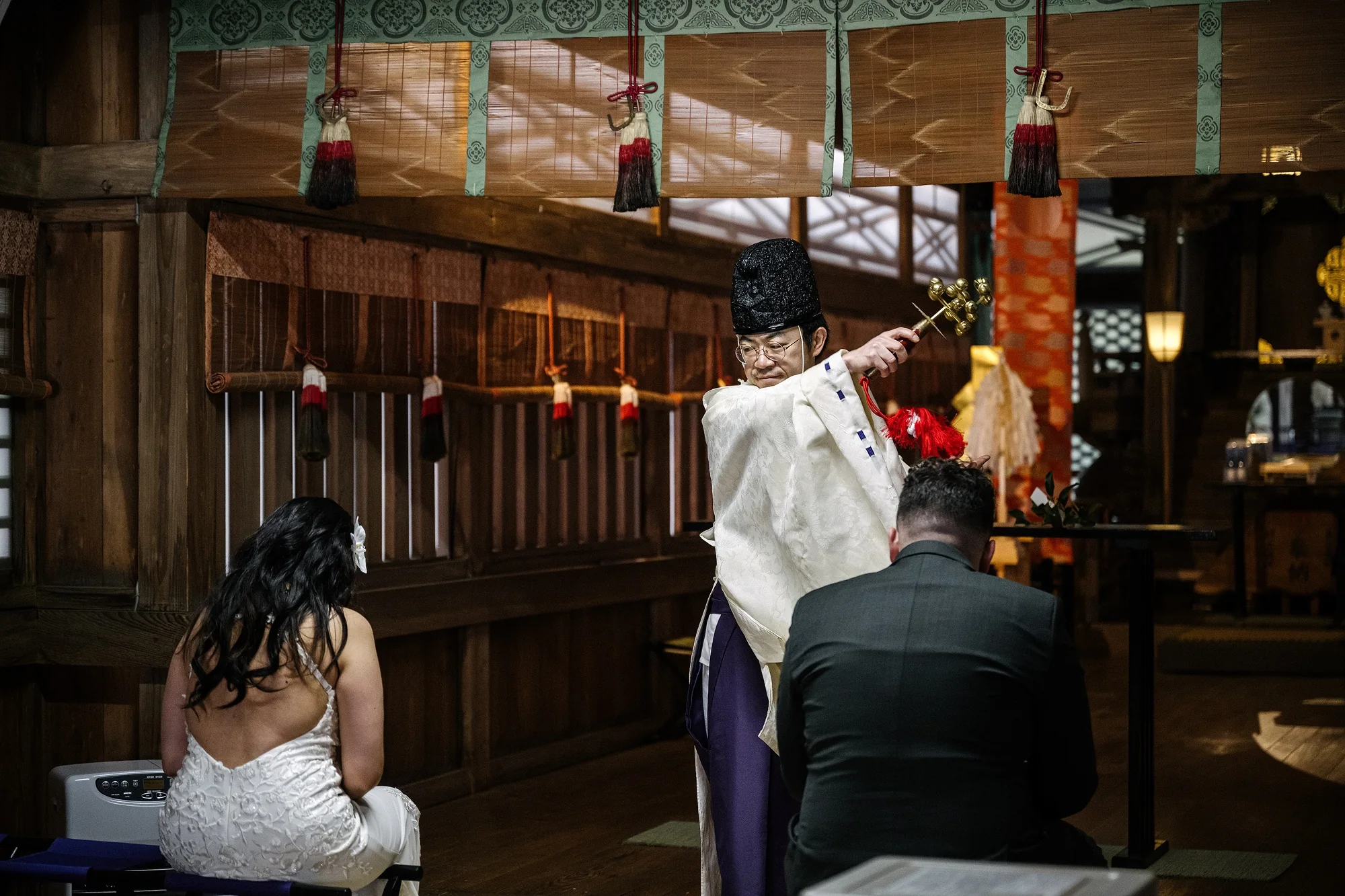 A priest waves the purification wand over the seated couple at a Sengen shrine near Mt Fuji, the bride in her wedding dress.