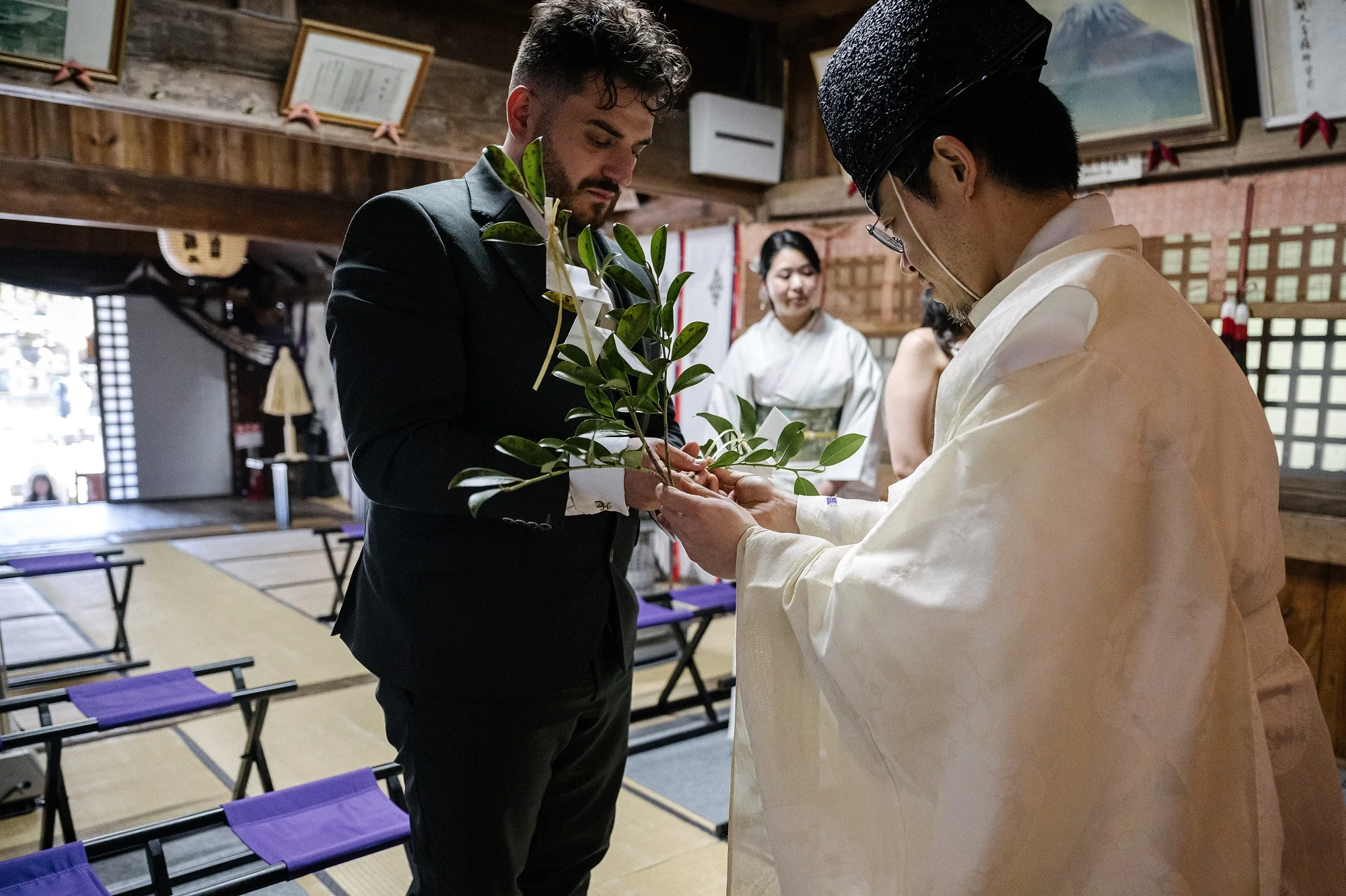 A priest hands the groom a tamagushi branch as the bride looks on during their blessing at a Sengen shrine near Mt Fuji.