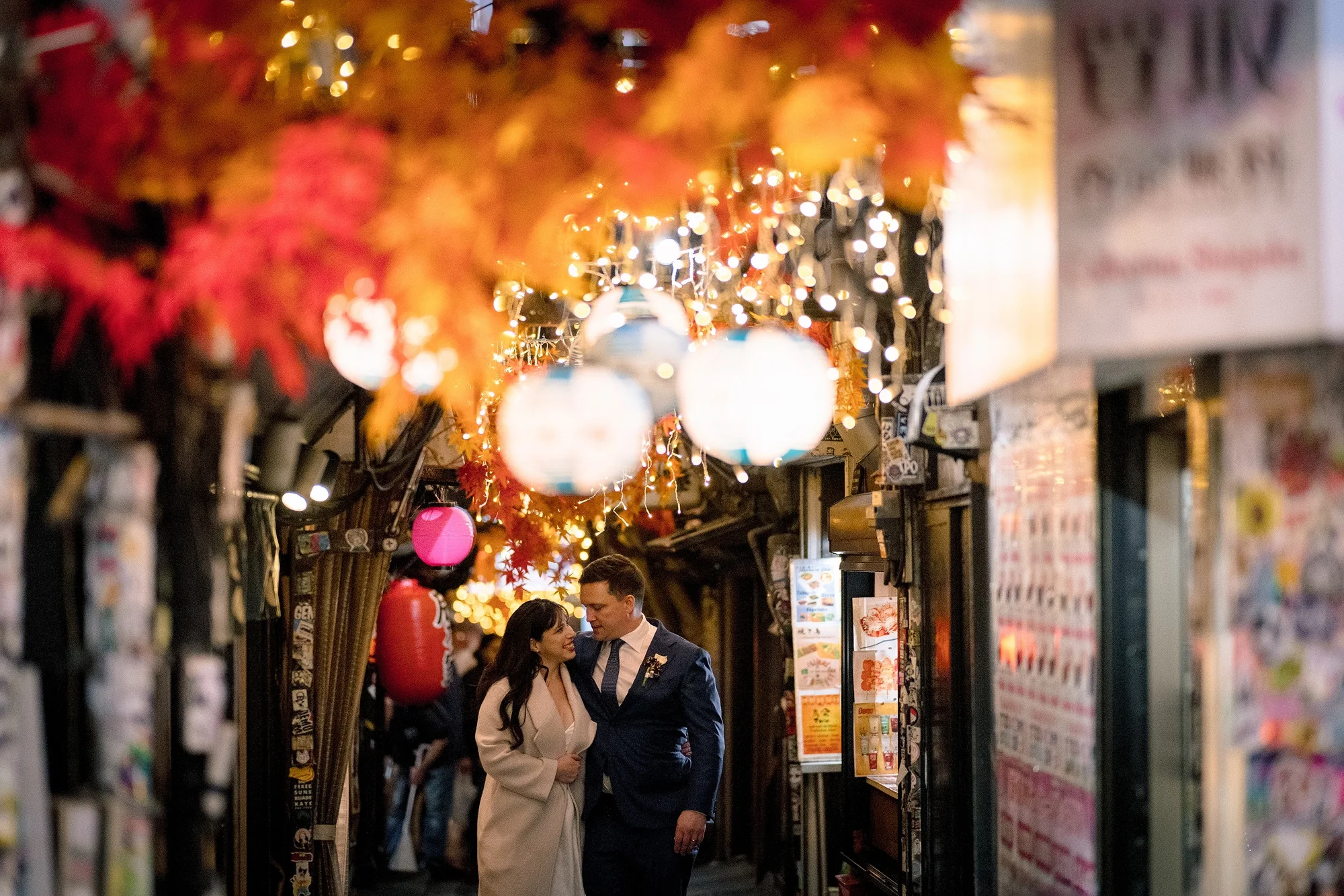 The couple stand among the red lanterns of Omoide Yokocho in Shinjuku at night.