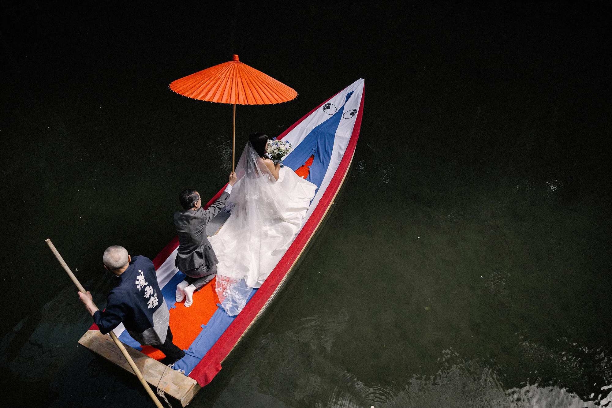 Seen from above, the couple cross a pond in a small boat under a red umbrella in Shuzenji, Izu.