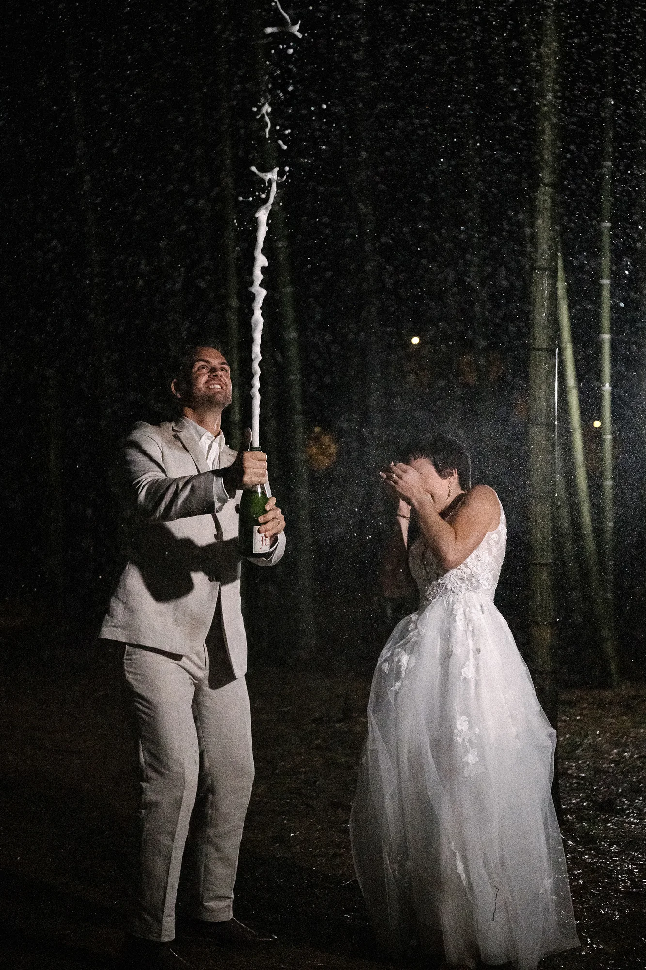 At night in the rain, the groom sprays champagne high into the air as the bride laughs in a bamboo grove in Tochigi.