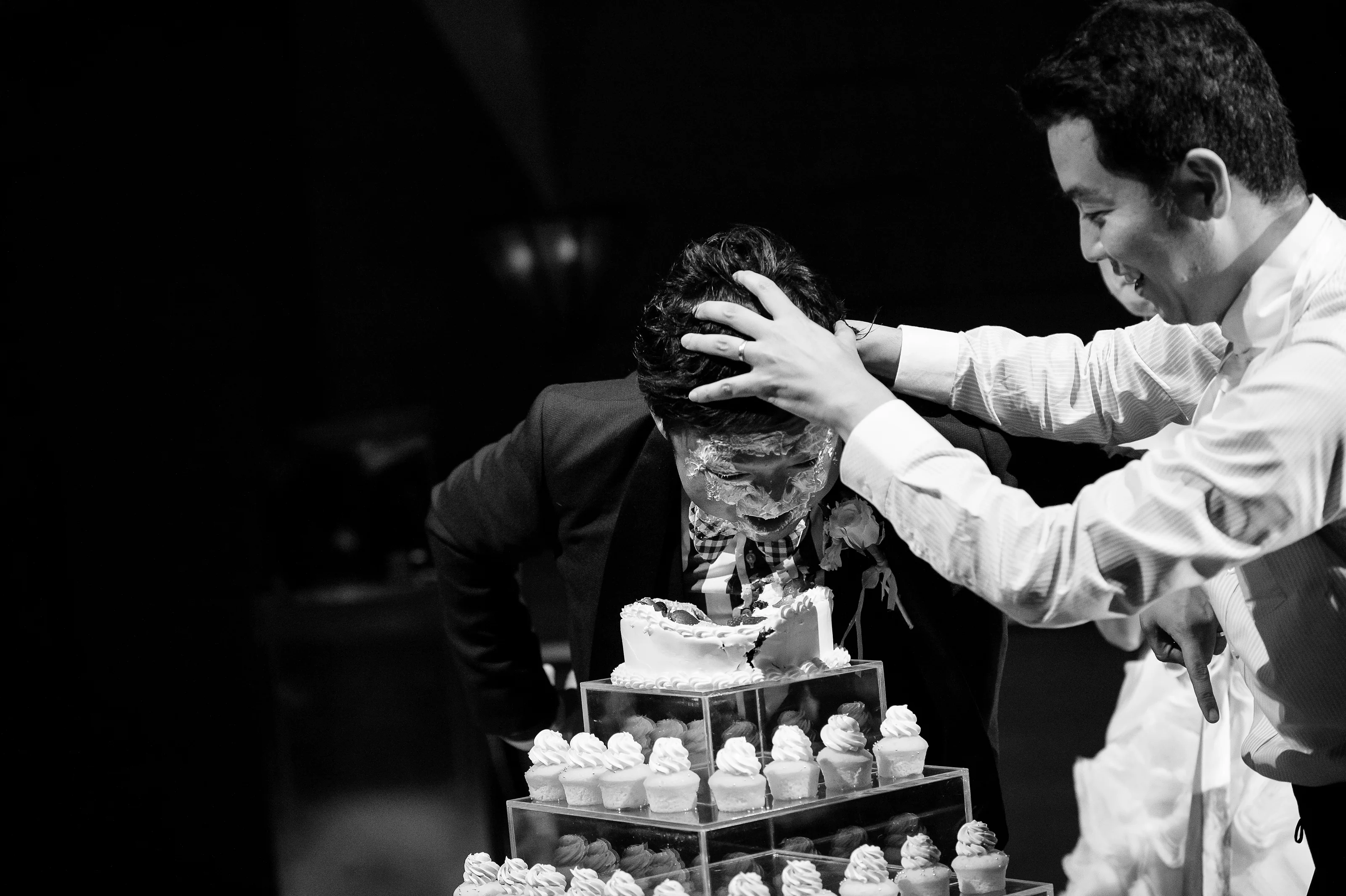 In black and white, a friend presses the groom's face into the cake at the Tokyo American Club.