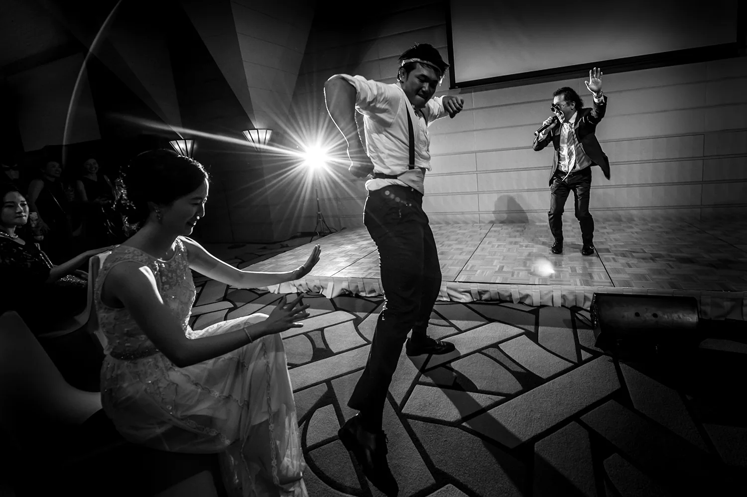 In black and white, the groom dances wildly as the bride and guests watch at the Tokyo American Club.