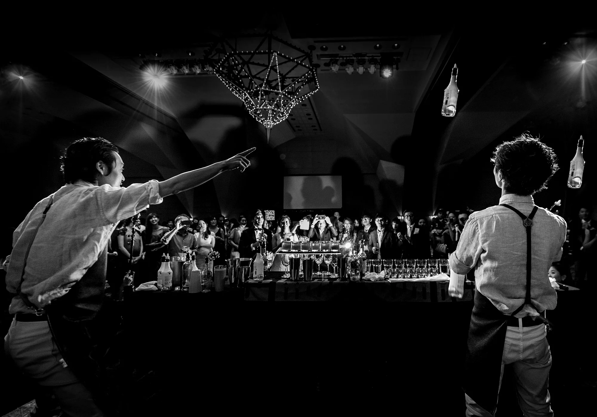In black and white, two guests raise their glasses to each other across a lit bar at the Tokyo American Club.