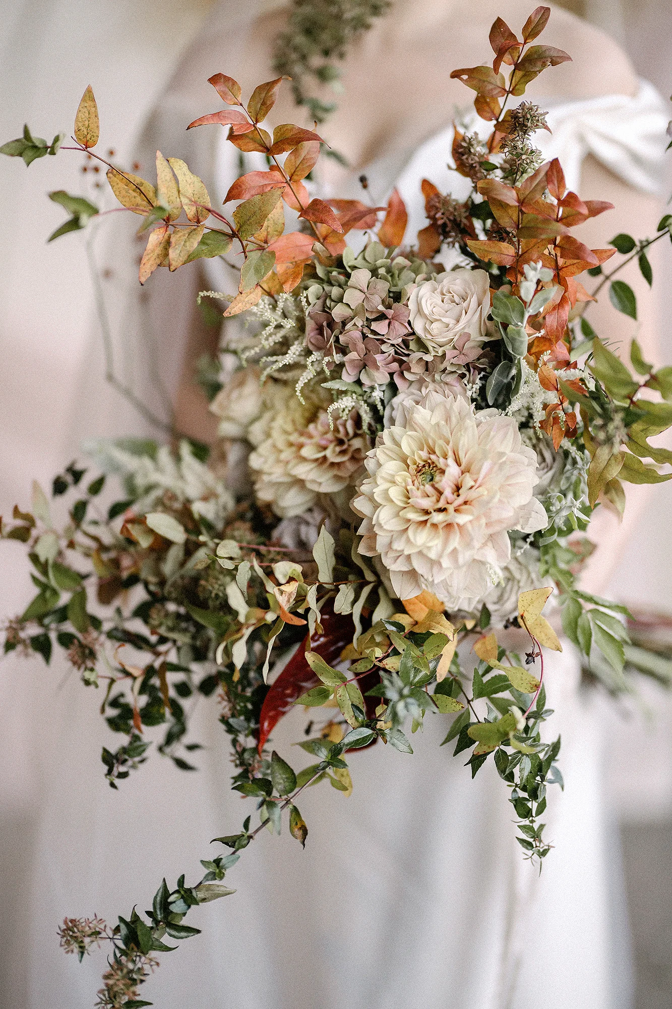 The bride holds a loose bouquet of dahlias, roses and autumn leaves against her gown in Tokyo.