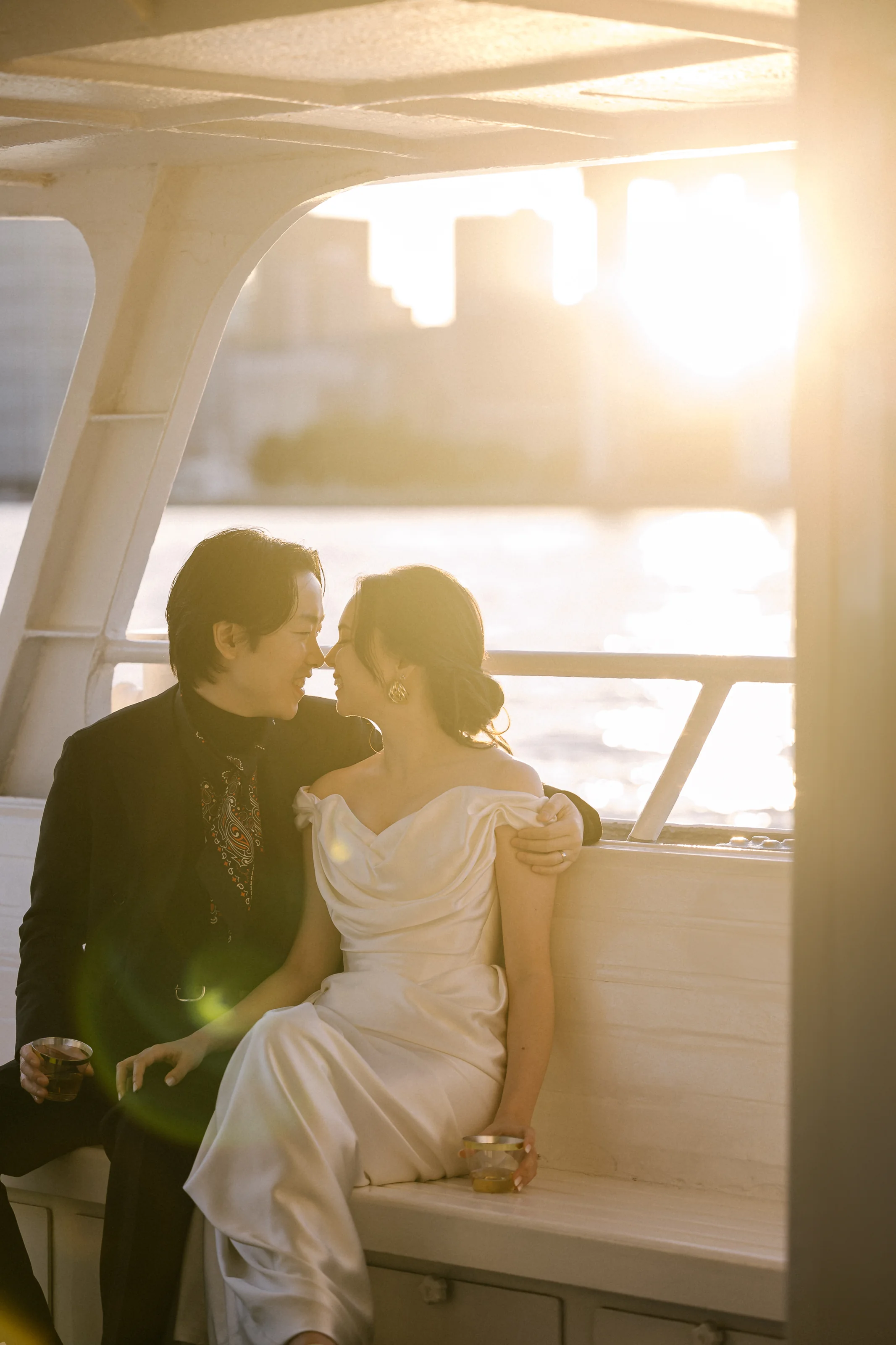 A couple sit close on the deck of a boat on Tokyo Bay as the sun sets behind them.