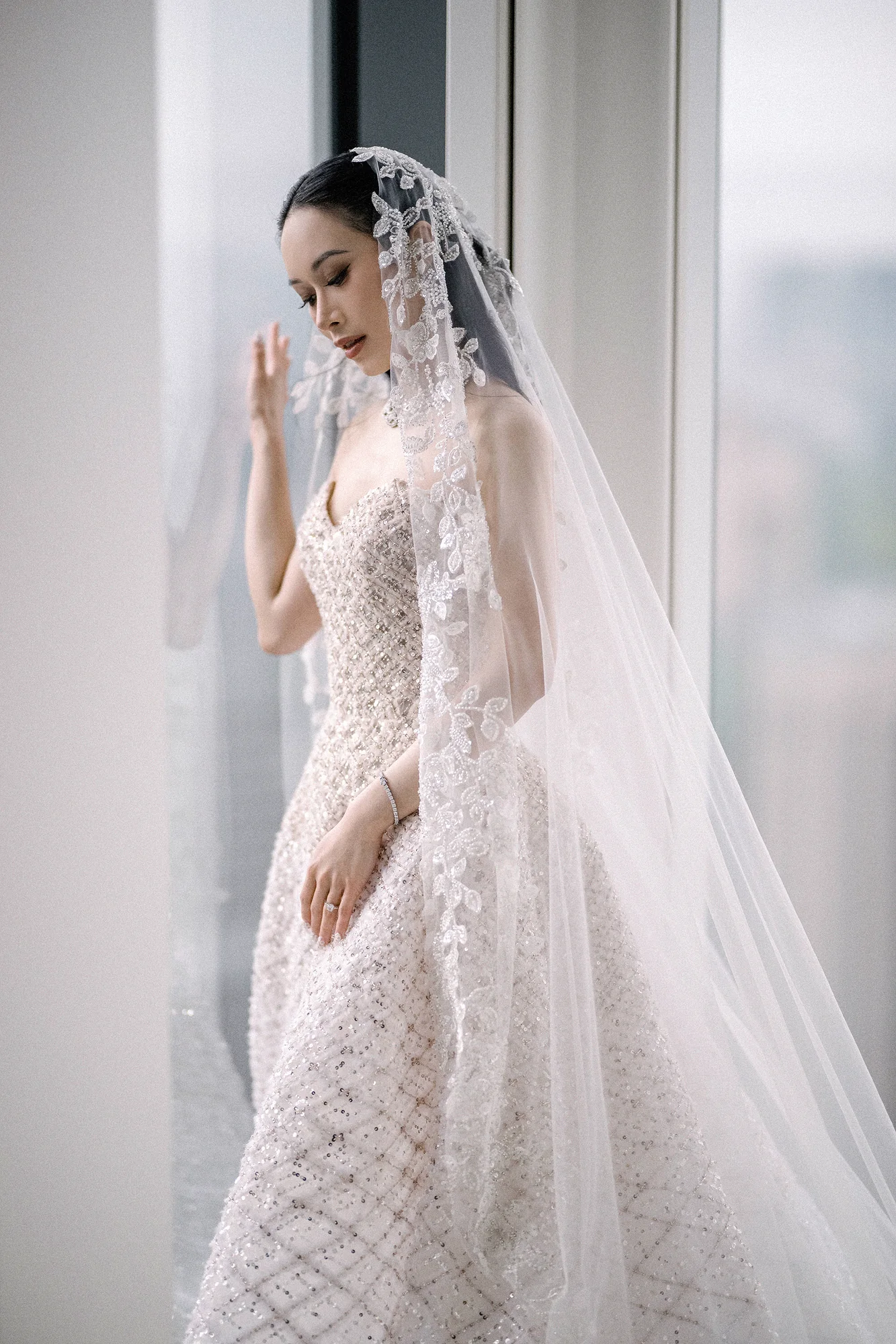 The bride stands at a tall window at Andaz Tokyo Toranomon Hills, her lace veil falling around her.