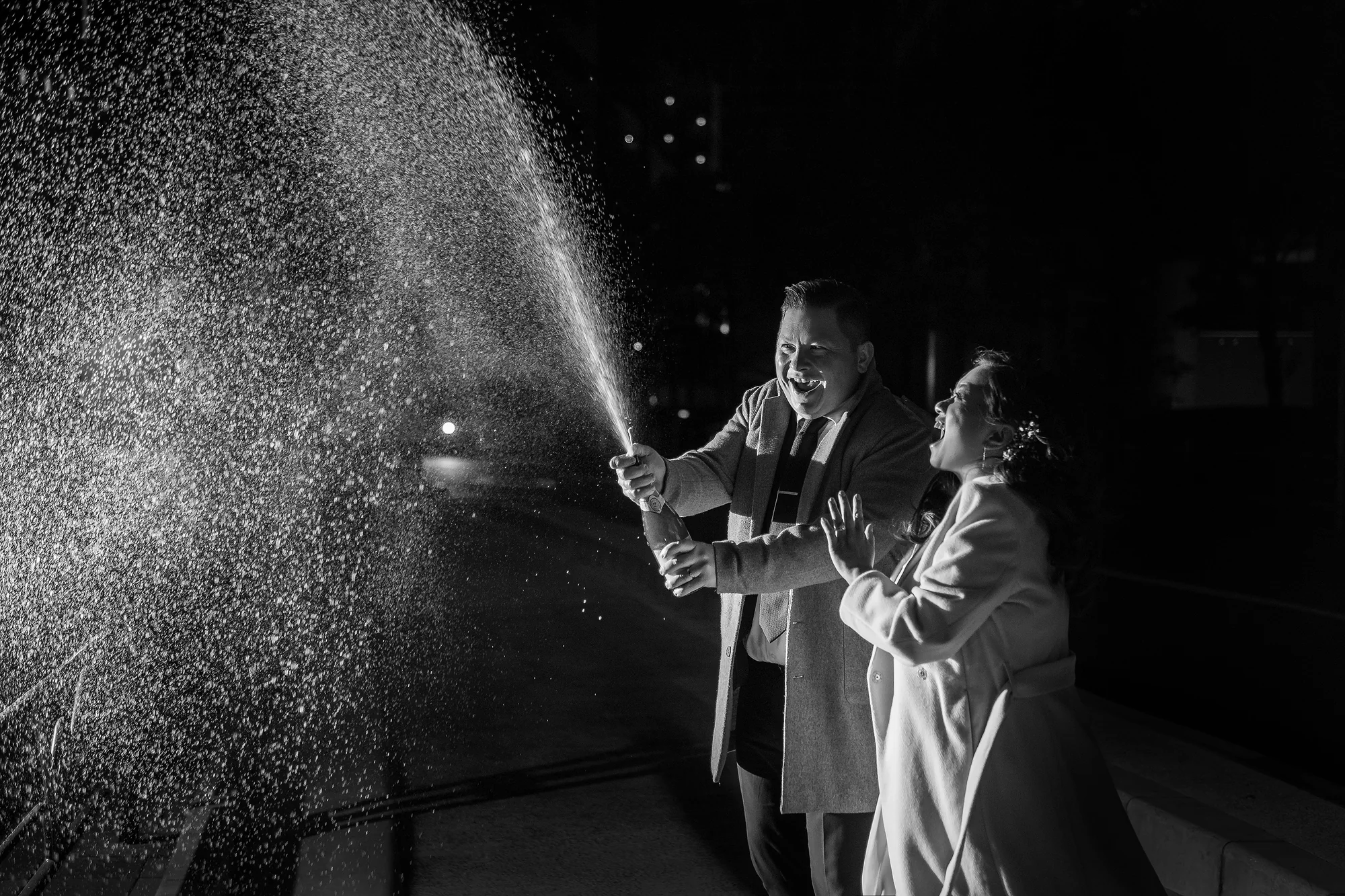 In black and white, the groom sprays champagne into the night as the bride laughs in Tokyo.