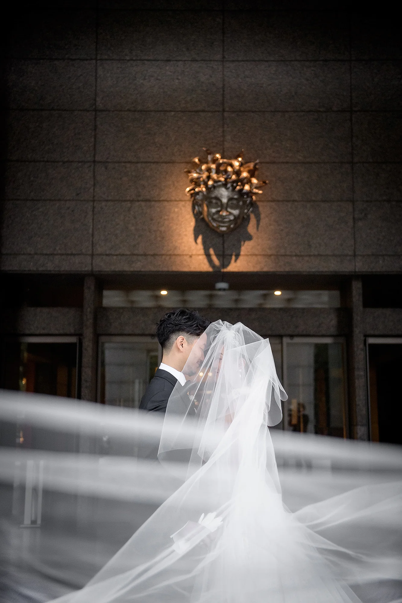 The bride's long veil sweeps through the frame as the couple stand at the end of a dark aisle in Tokyo.