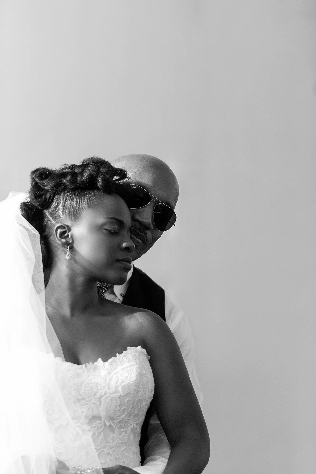 In black and white, the groom holds the bride close from behind, her eyes closed, in Tokyo.