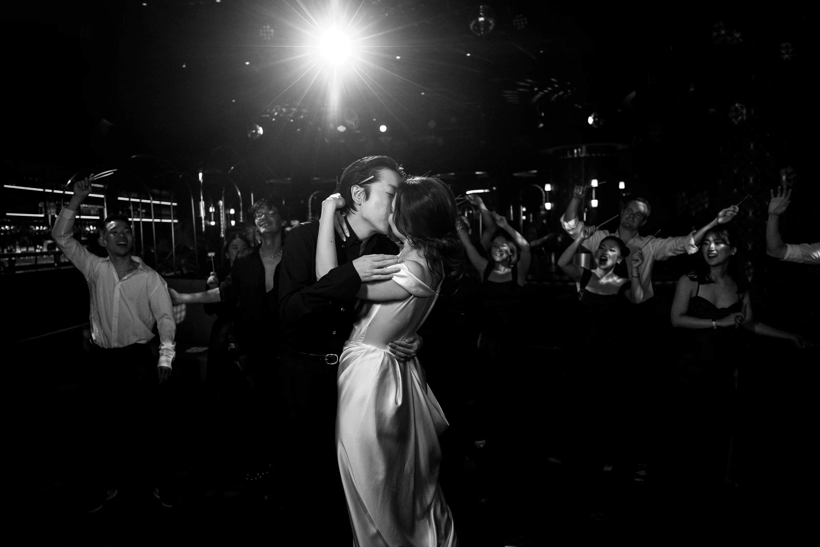 In black and white, the couple kiss on a crowded dance floor as a light flares above their guests in Tokyo.