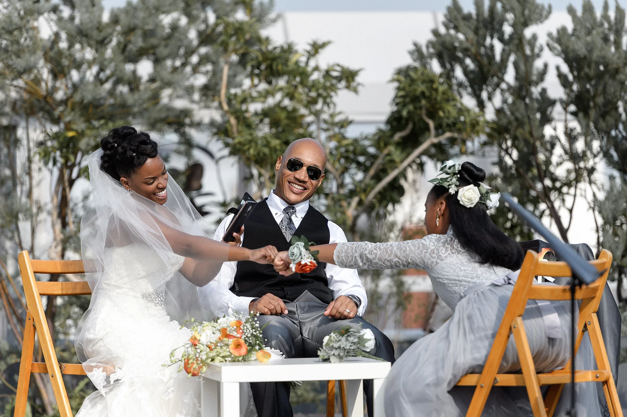 The couple and a young girl join hands at a small table during their outdoor ceremony in Tokyo.