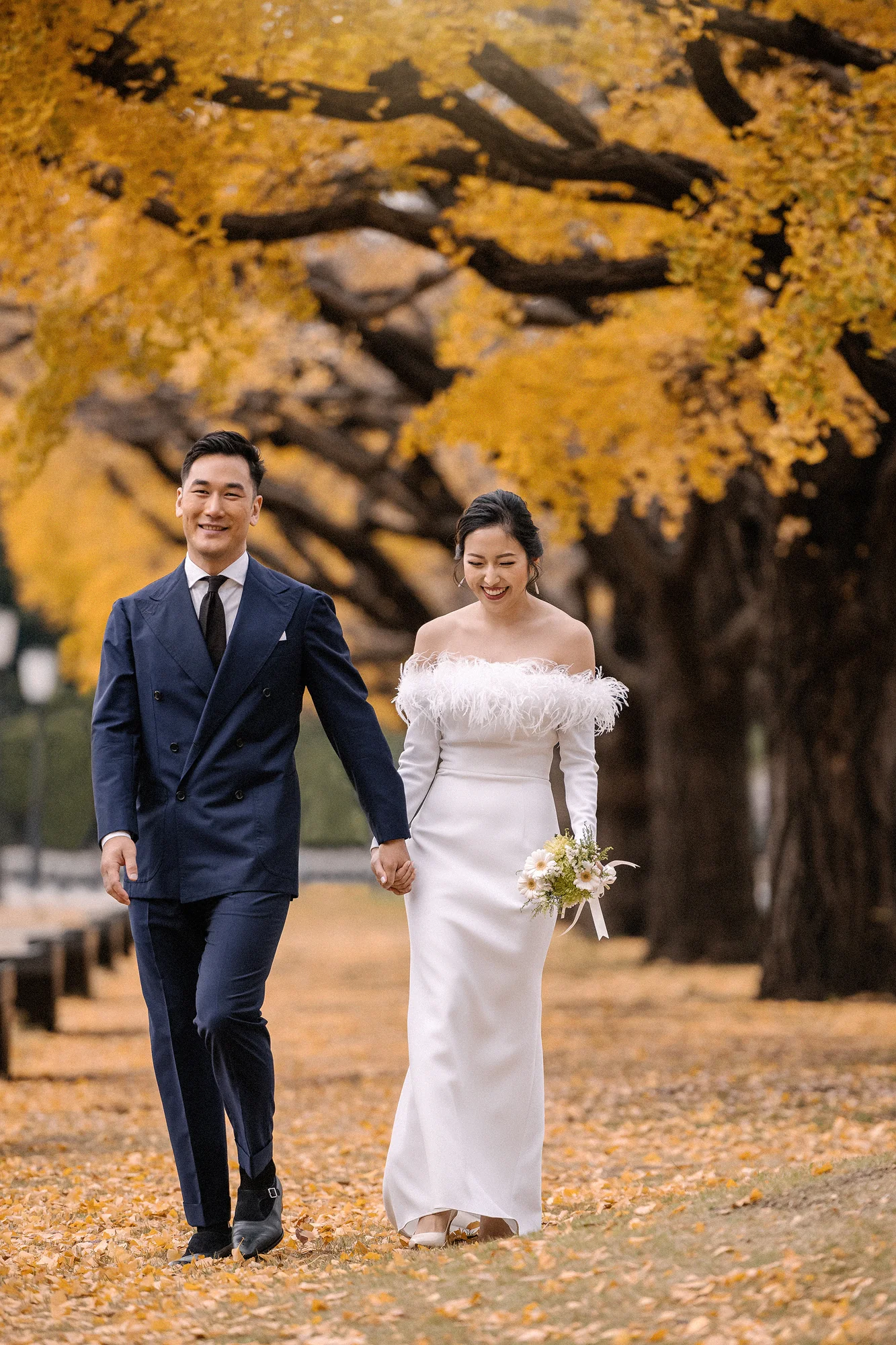 The couple walk hand in hand down an avenue of golden ginkgo trees in Tokyo.