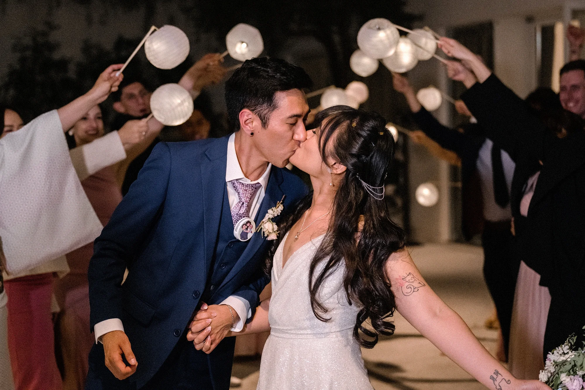 The groom kisses the bride beneath glowing paper lanterns as their guests celebrate in Tokyo.