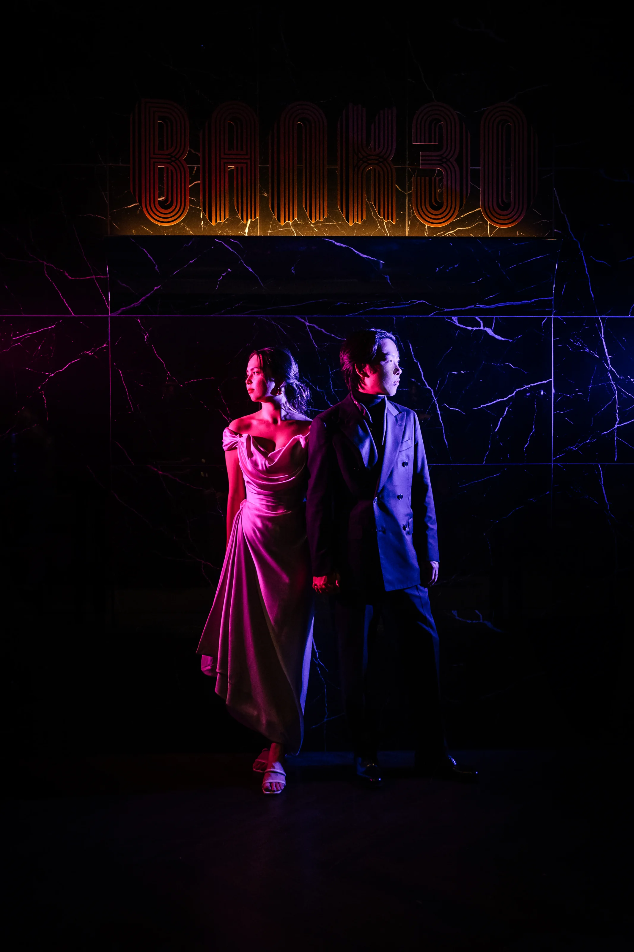 The couple stand in pink and blue light beneath a neon sign at a bar in Tokyo.
