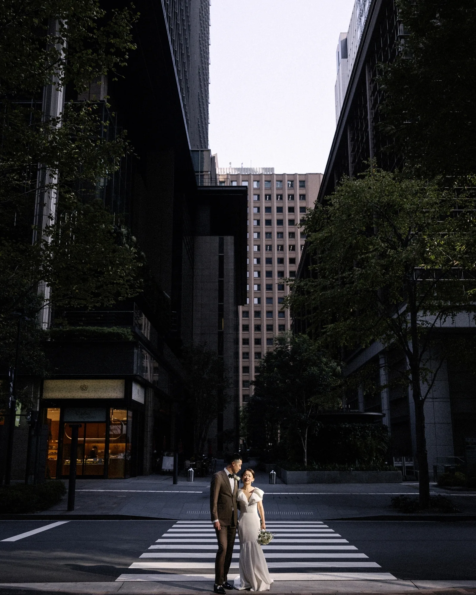 A couple stand small between tall city buildings in Tokyo.
