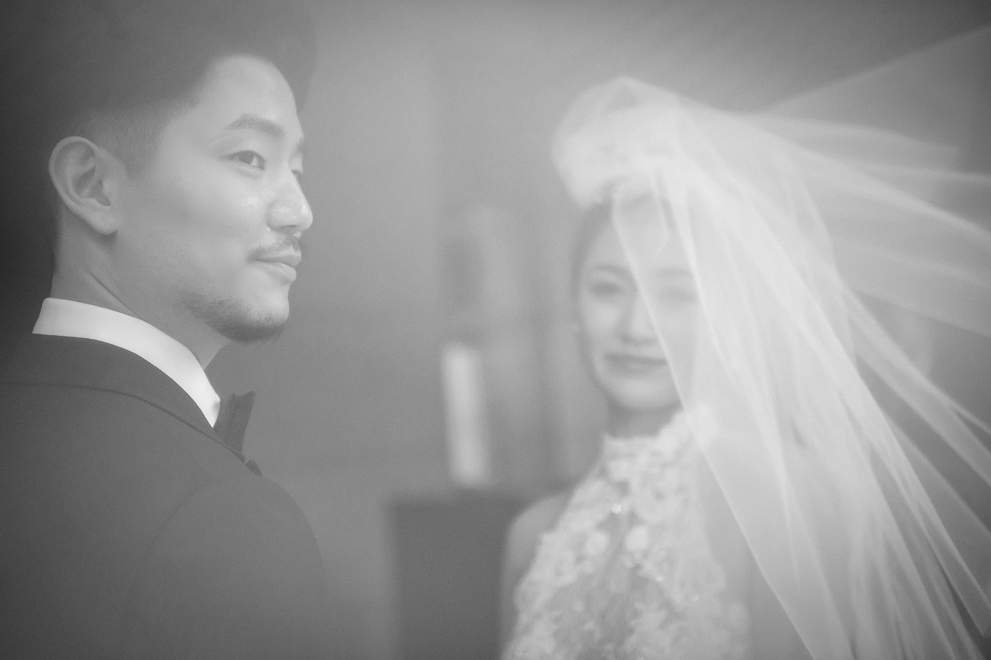 In soft black and white, the groom looks across at the bride through her veil in Tokyo.