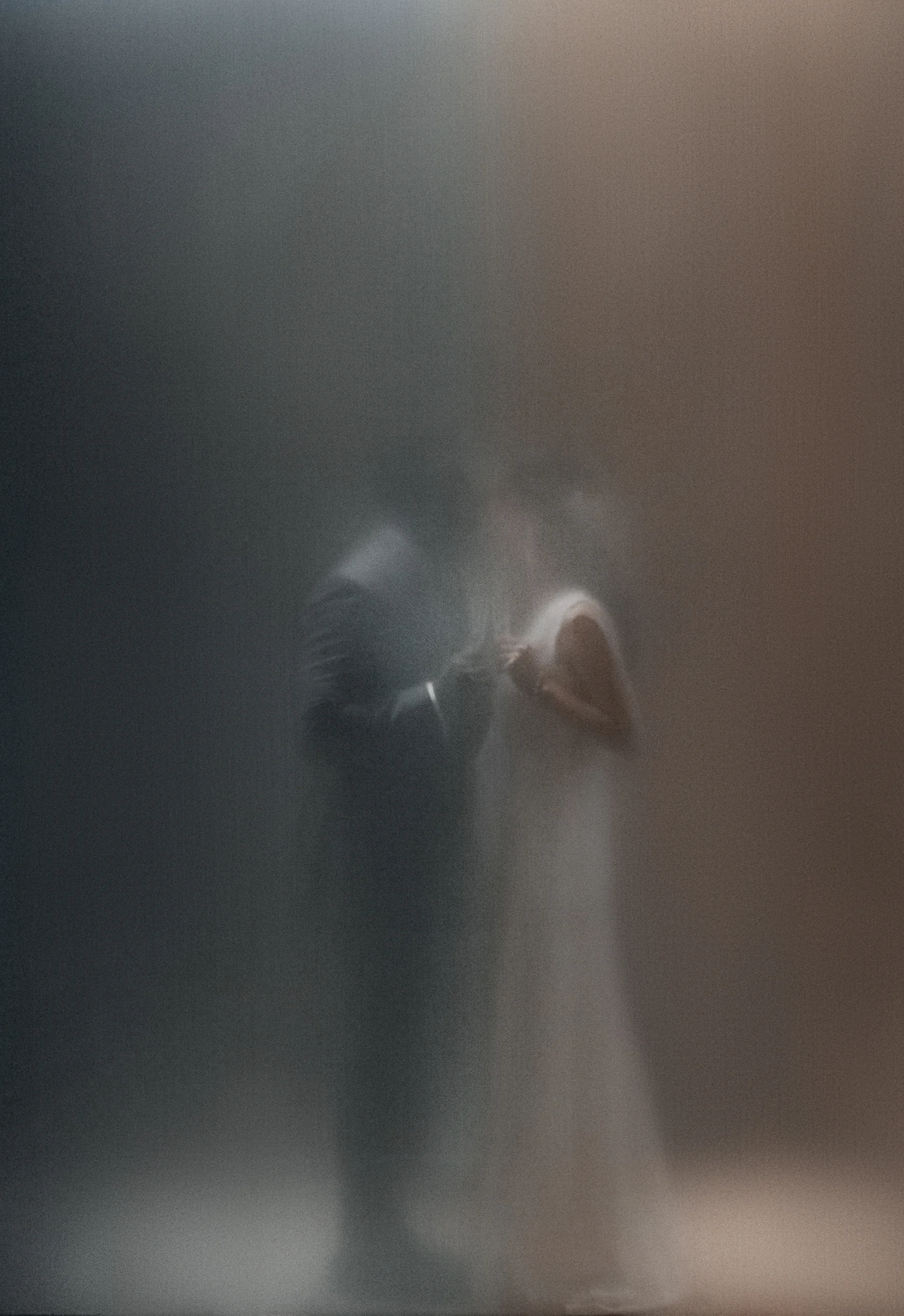 A couple, softly blurred, hold each other behind a veil of mist and pale light in Tokyo.