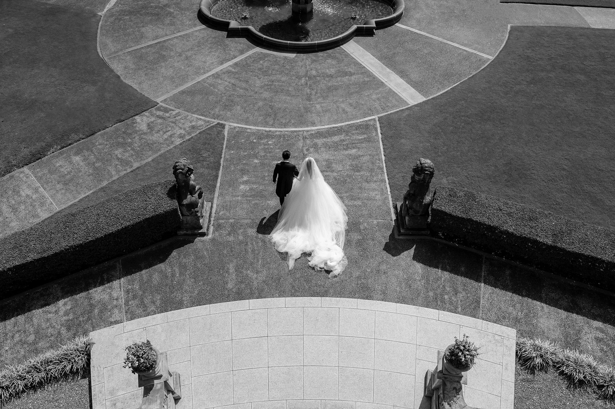 In black and white, seen from above, the bride and groom walk across the forecourt of the Tsunamachi Mitsui Club in Tokyo.