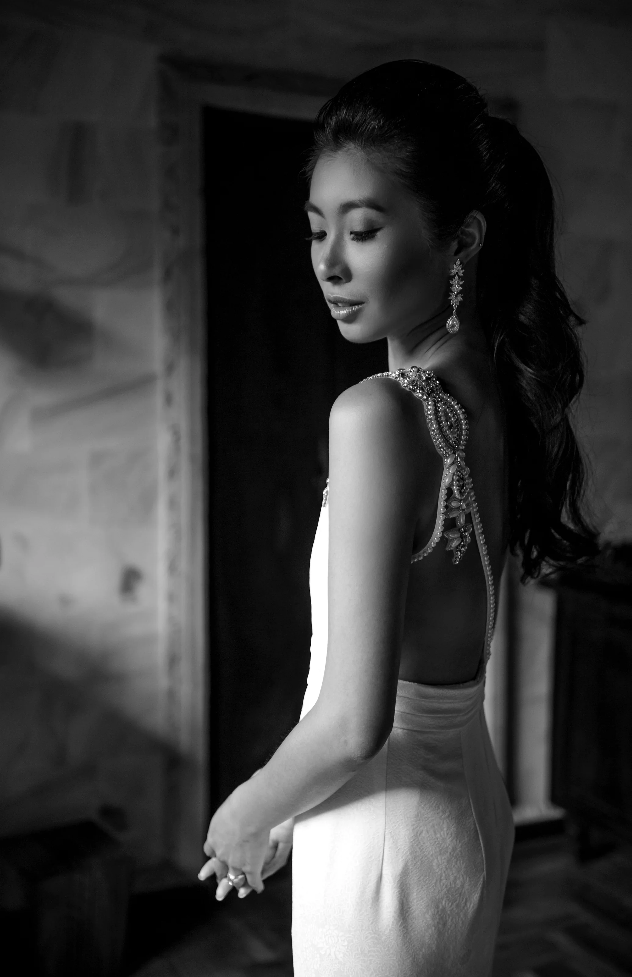 In black and white, the bride looks over her shoulder in soft window light in Ubud, Bali.