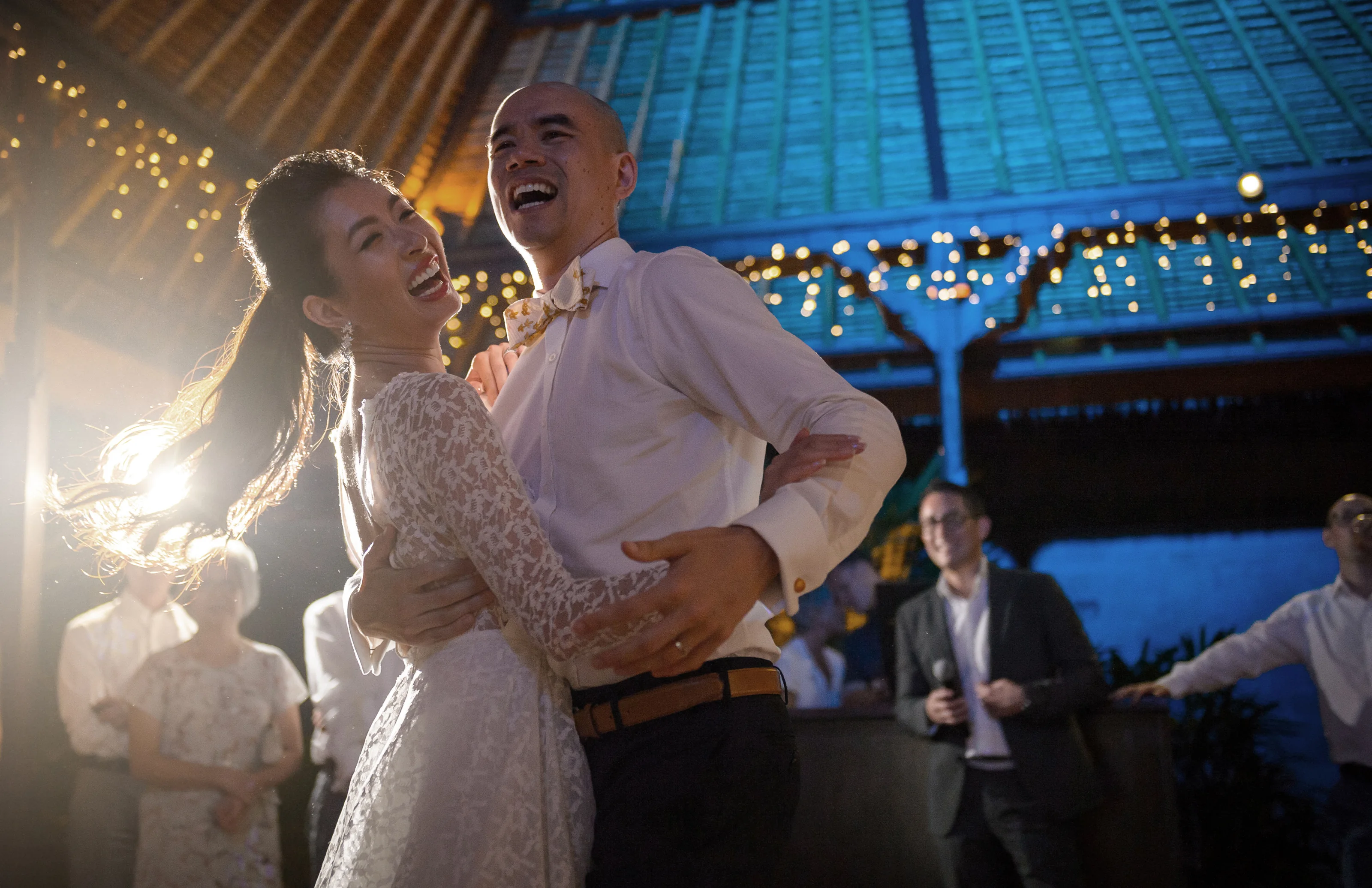 The bride laughs as the groom lifts her into a dance under strings of lights at Royal Pita Maha in Ubud.