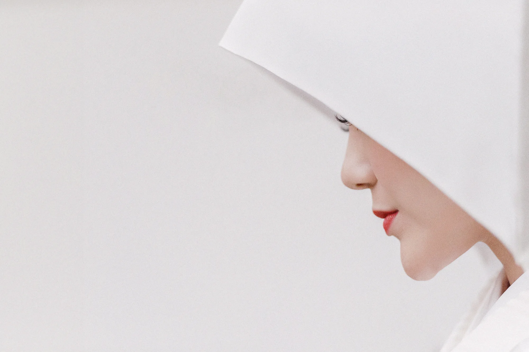 A bride in a white wataboshi hood in profile, her red lips the only color.