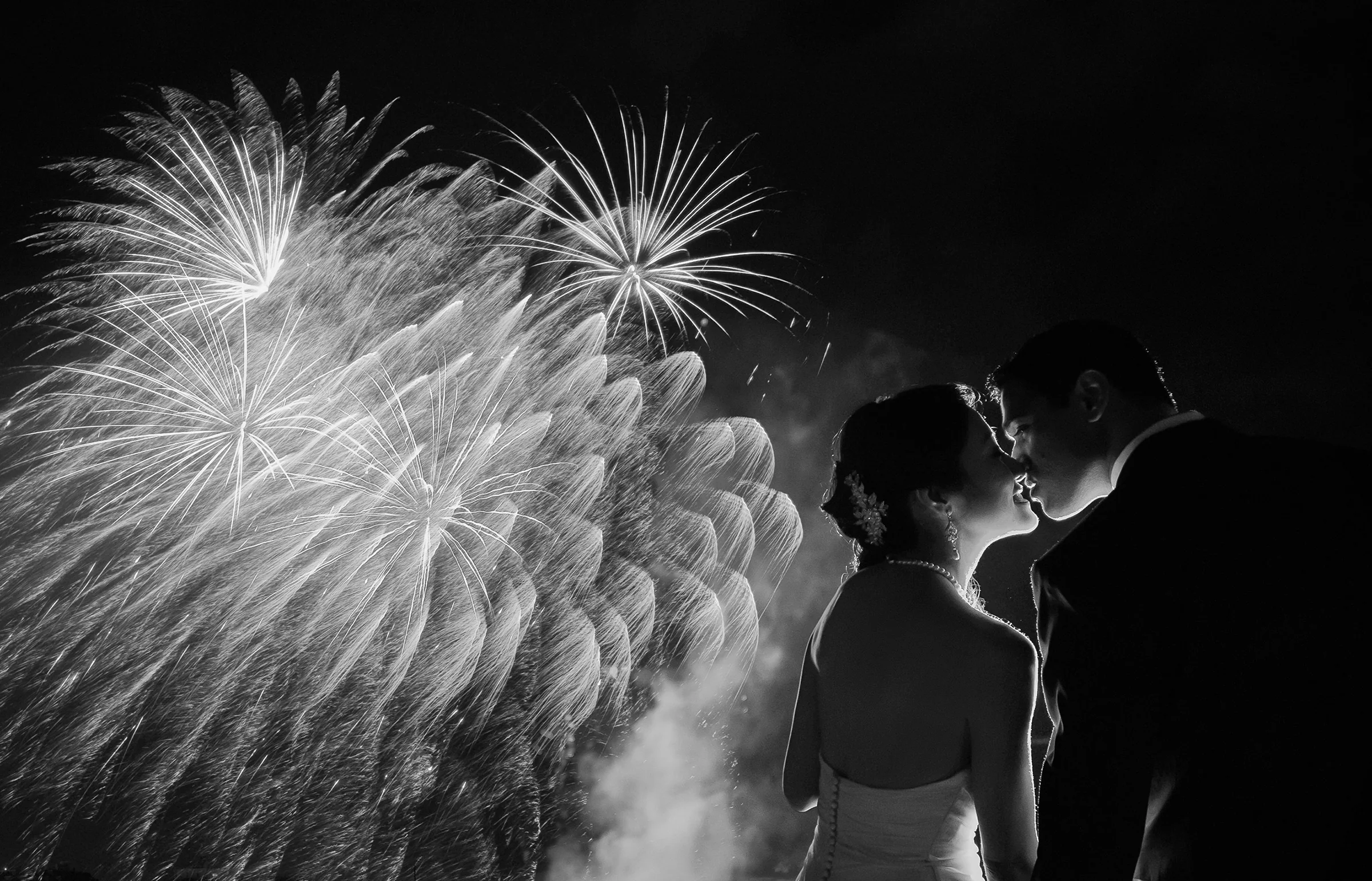 In black and white, the couple kiss as fireworks burst behind them.