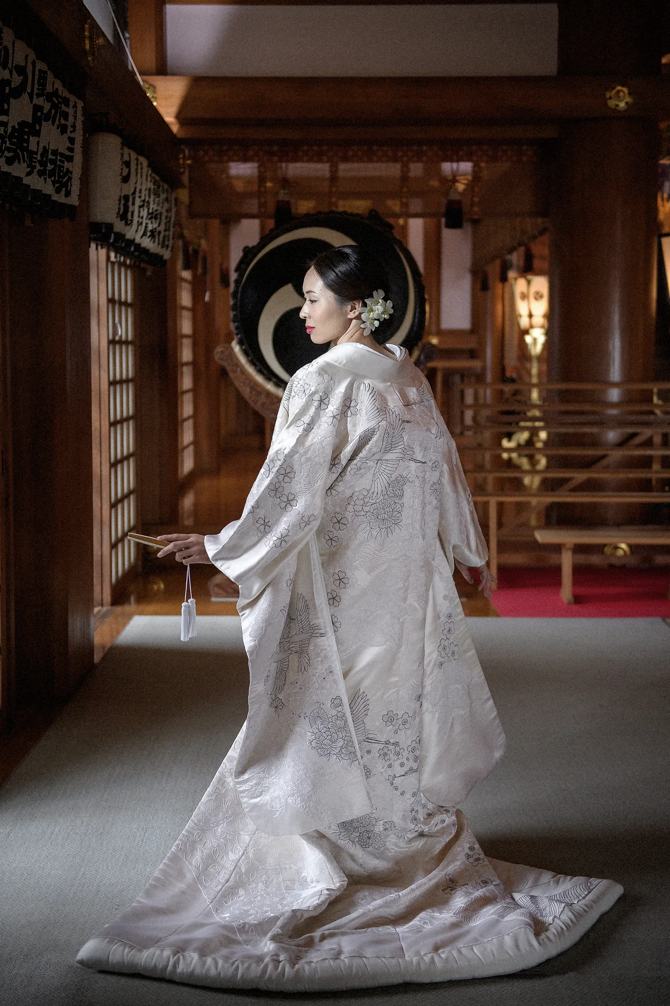 A bride in a white uchikake stands in a shrine hall beside a taiko drum.
