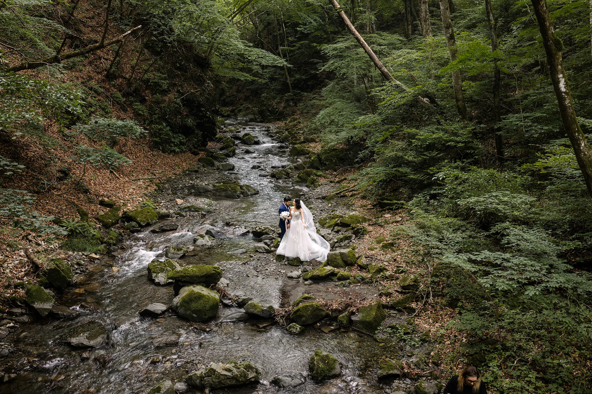 The couple walk beside a mountain stream through green forest in Yamanashi.