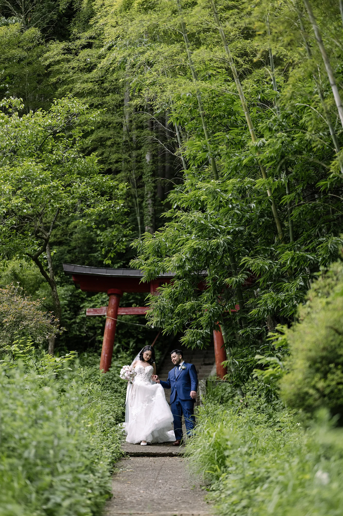 The couple walk up a path through red torii into the forest above a Yamanashi village.